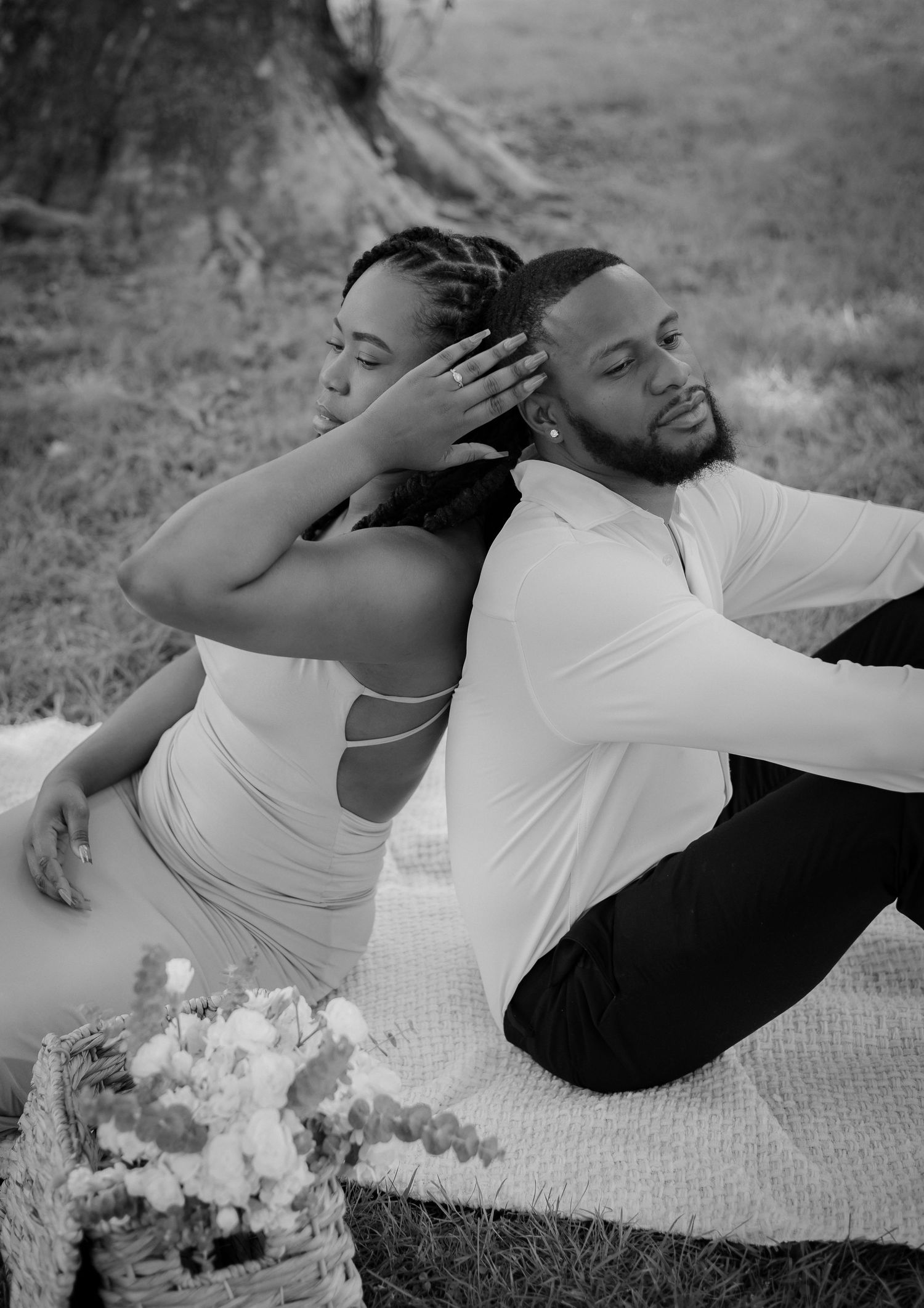 Black and white photo of Black couple sitting back-to-back on blanket with flower basket nearby.