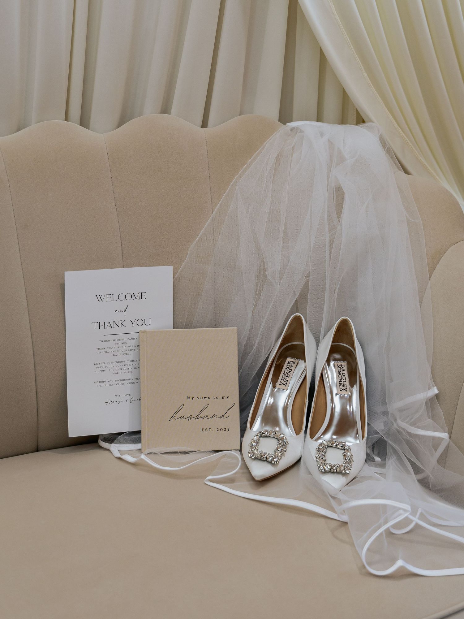 Bridal heels, veil, vow book, and welcome card arranged on beige chair for Muslim wedding.