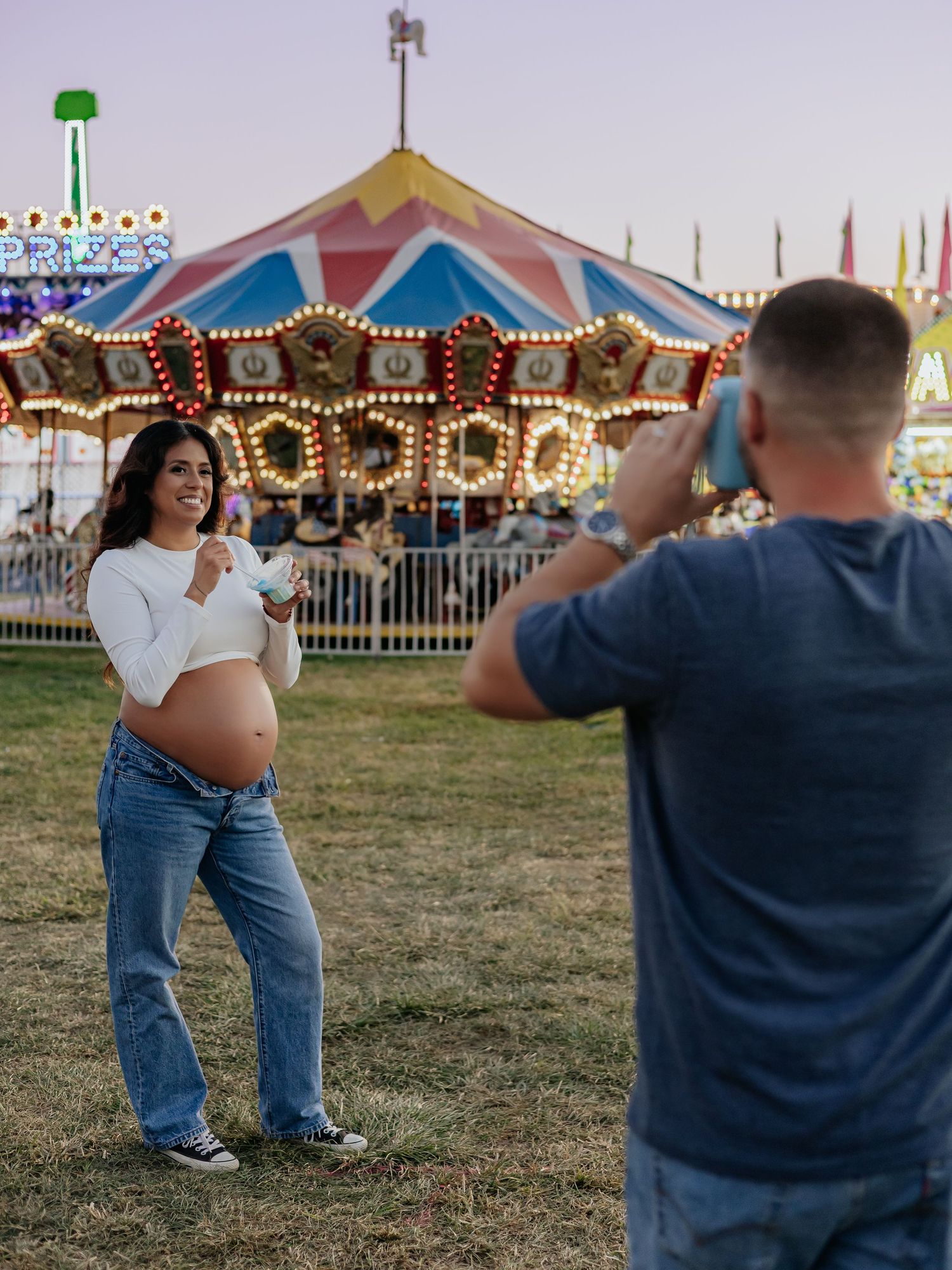 Man taking photo of smiling pregnant woman at colorful carnival.