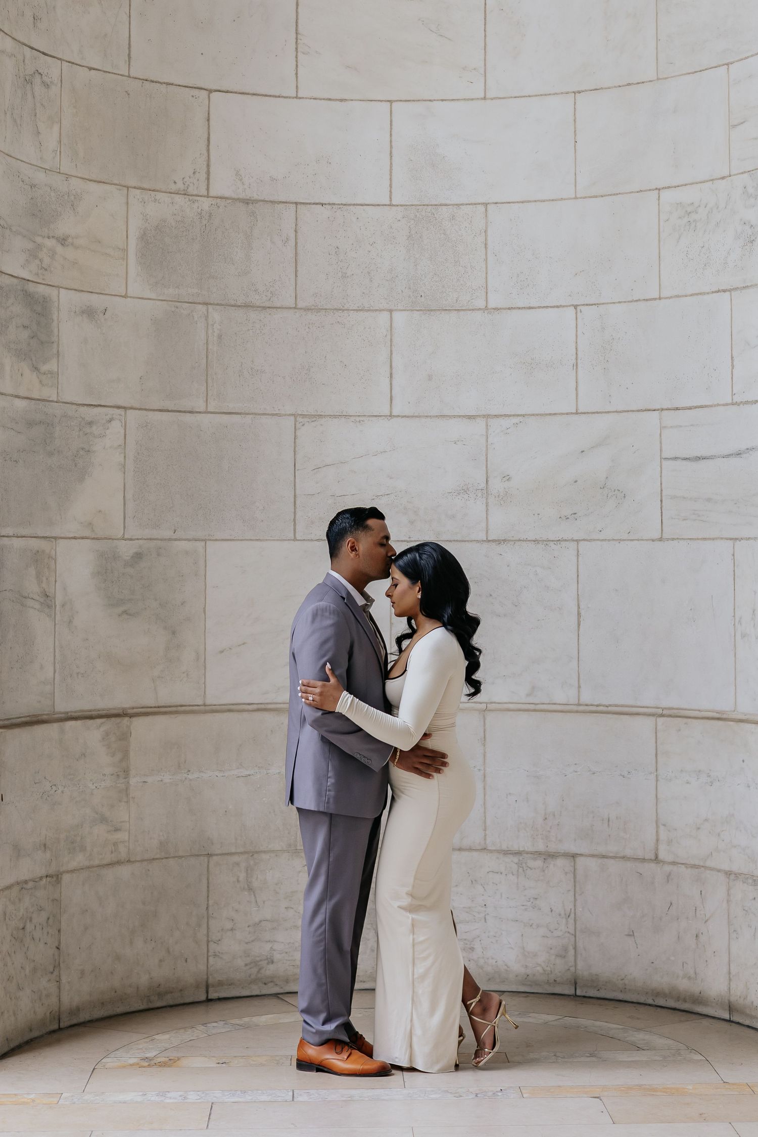 Couple sharing a romantic embrace against a curved stone wall during their engagement photo session.