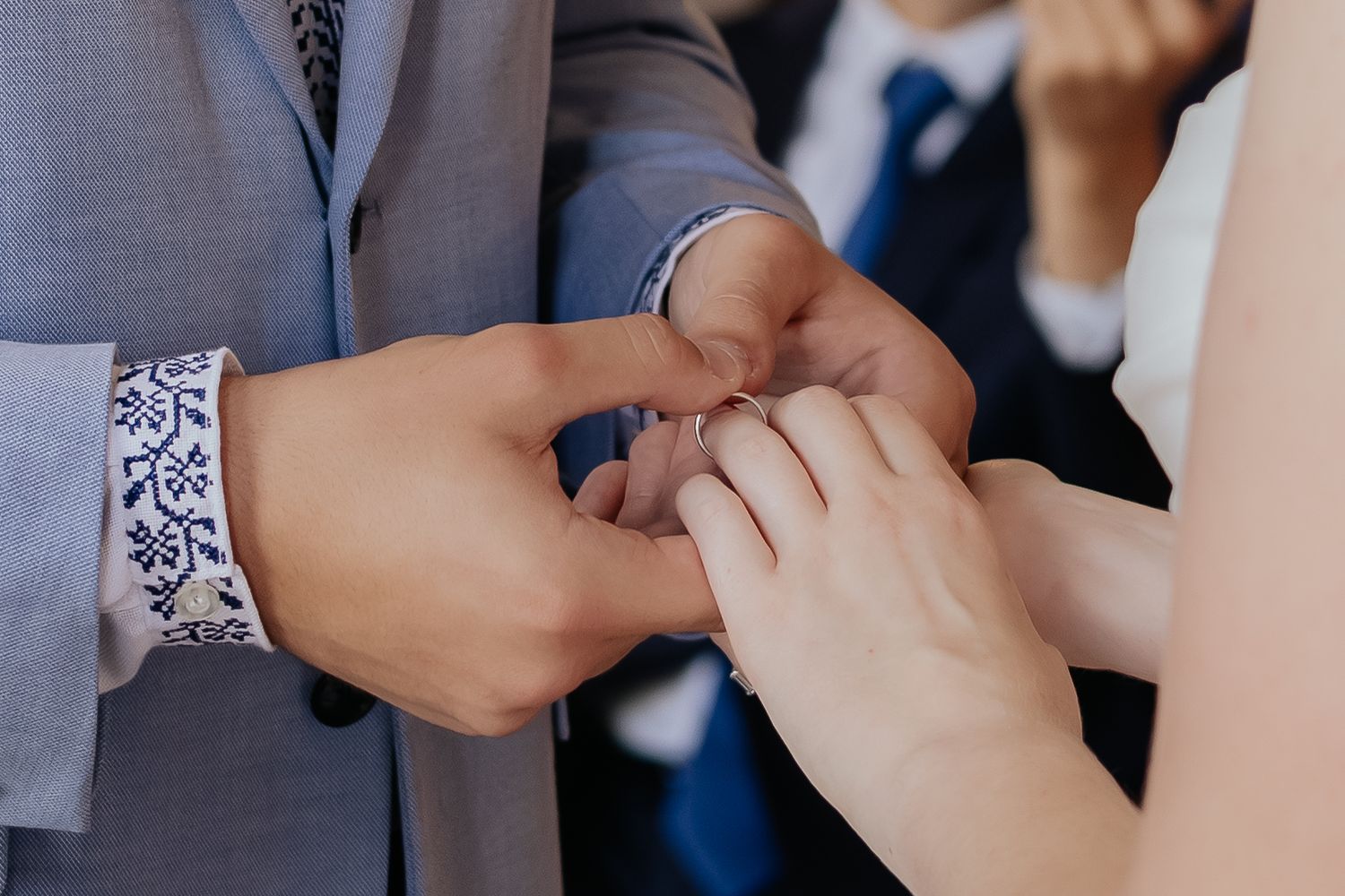 Groom placing a wedding ring on bride's finger during ceremony, close-up of hands.