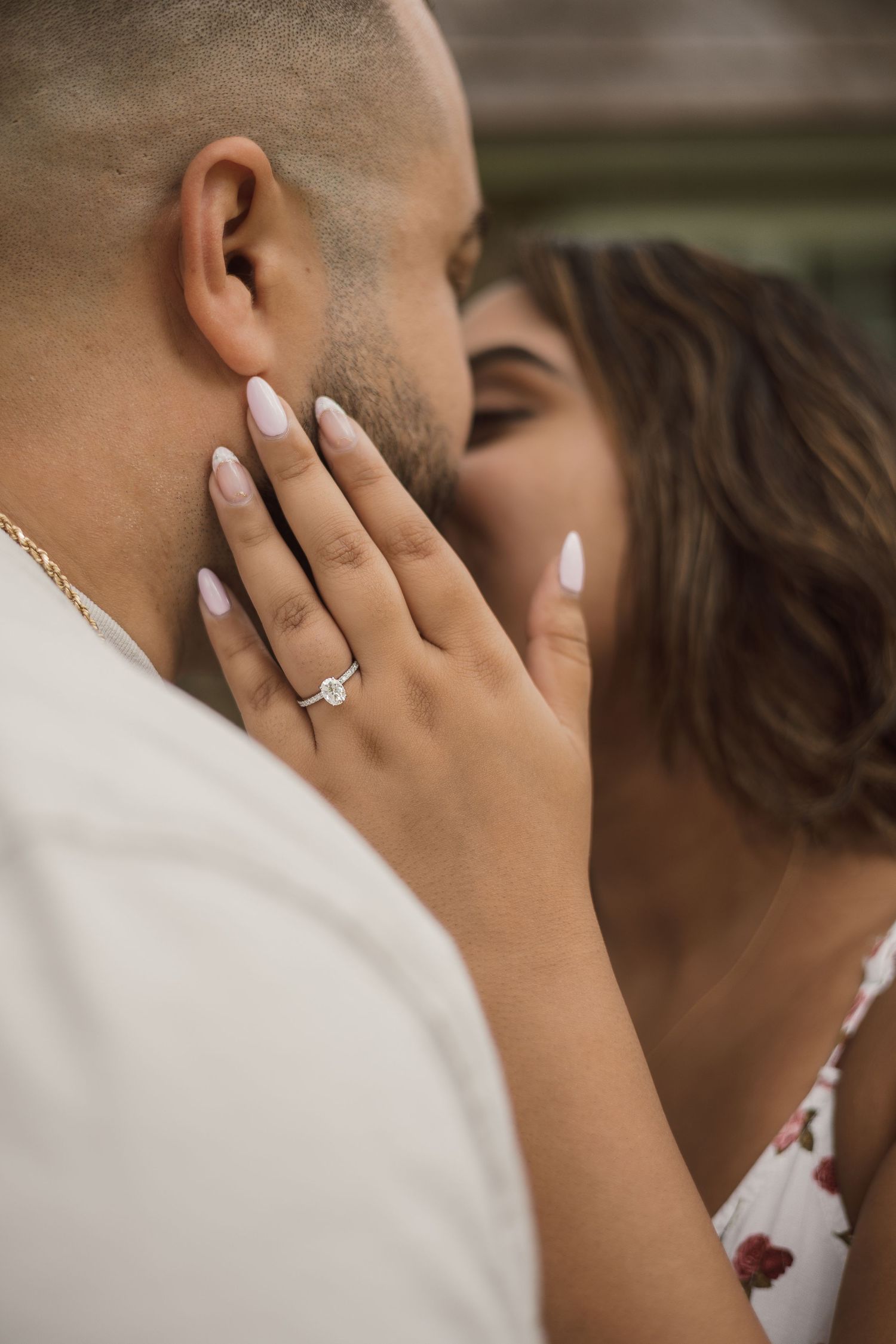 Close-up of an engaged woman with manicured nails and diamond ring tenderly touching her partners face.