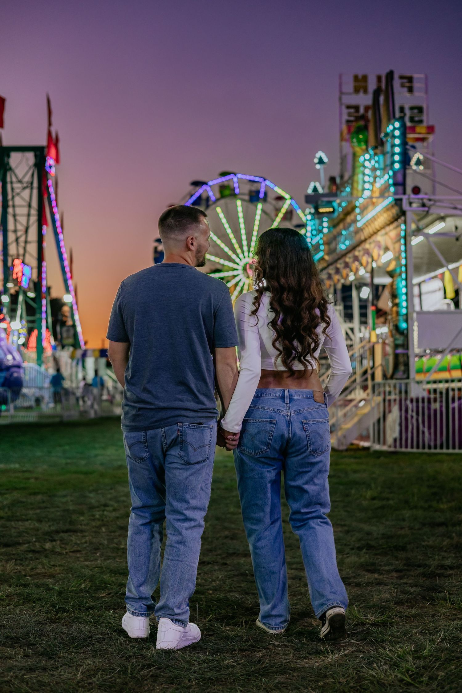 Couple holding hands viewing ferris wheel at carnival during sunset.