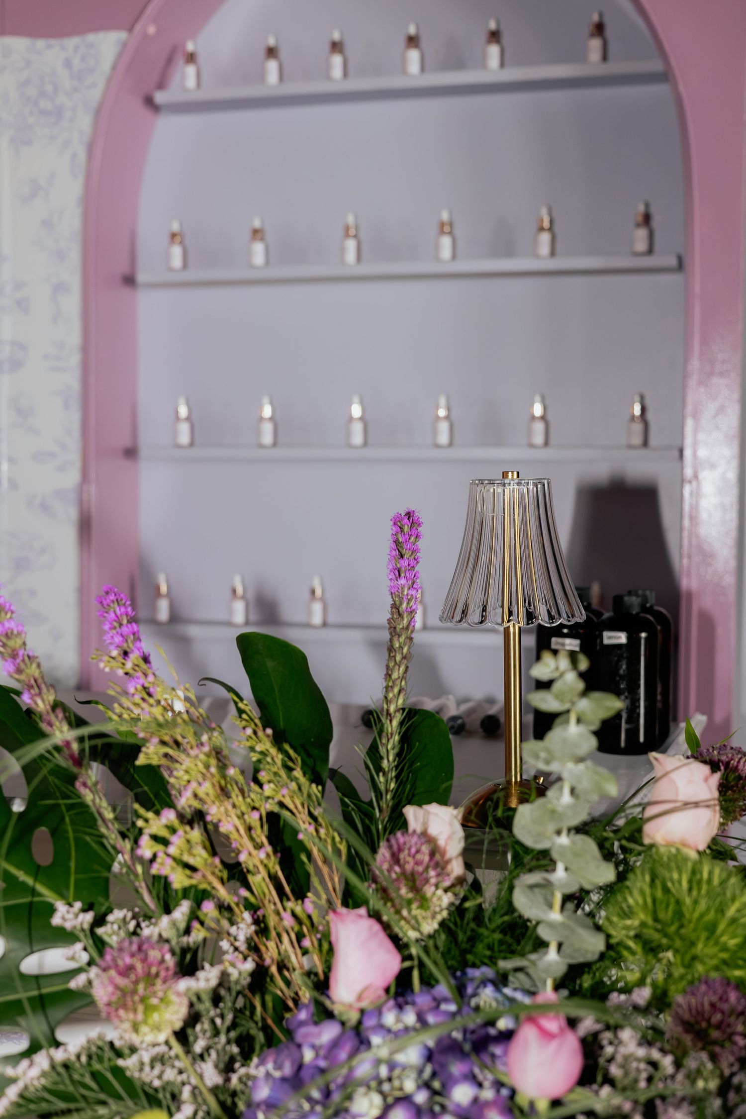Elegant floral arrangement with pink roses and purple wildflowers beside a gold lamp in a pink boutique.