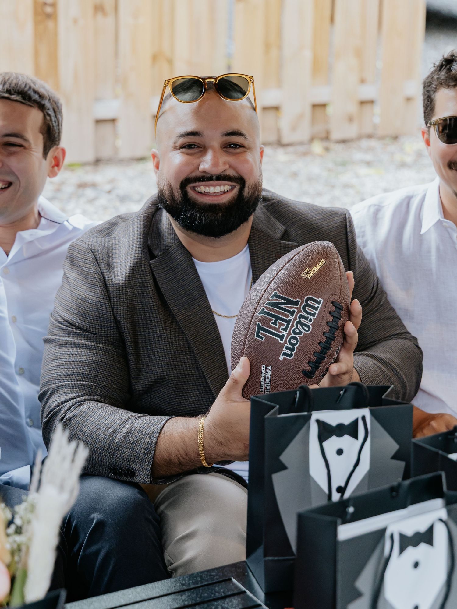 Smiling man holding Wilson NFL football at an outdoor groomsmen proposal gathering.
