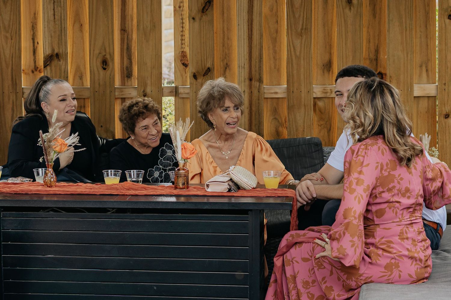 Four women sitting at a table chatting at an indoor event with wooden walls.