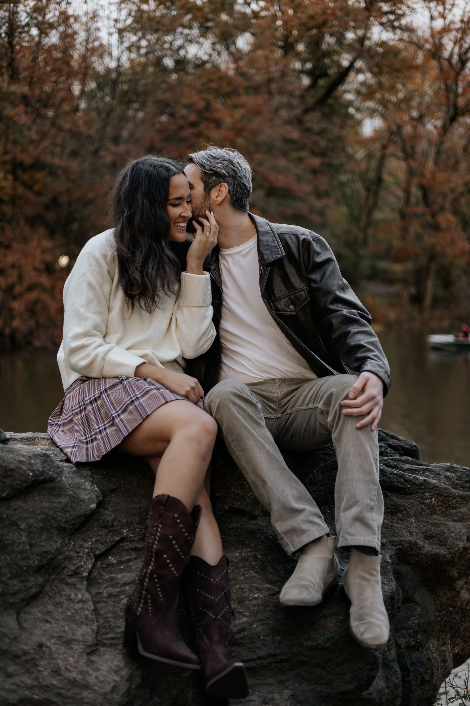 Couple sitting closely on rocks in Central Park, sharing an intimate moment amid autumn foliage.
