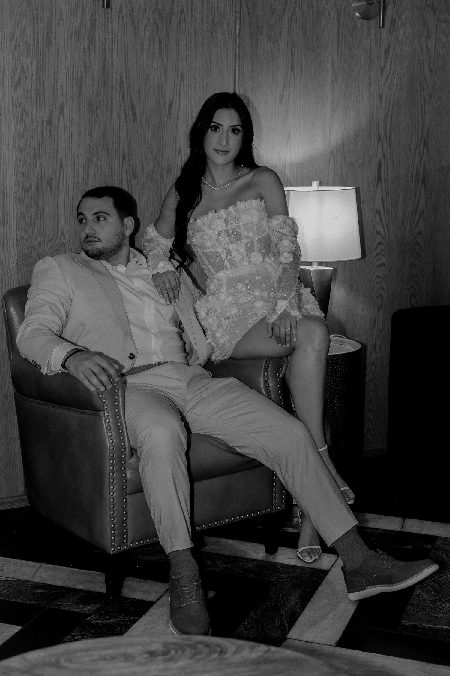 Black and white portrait of an elegant couple posing in a warmly lit room with wood paneling.