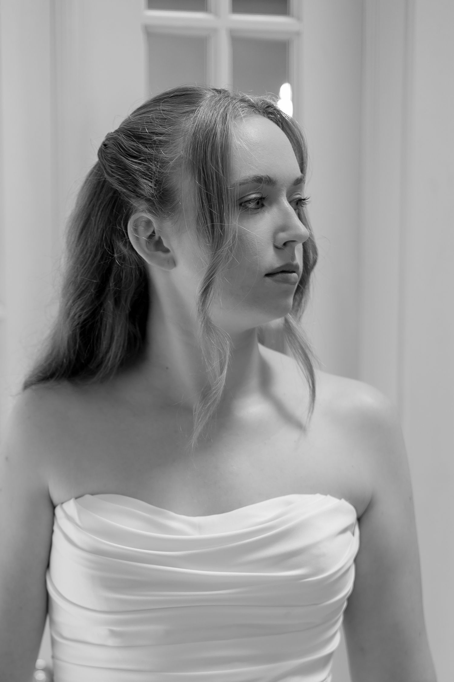 Elegant black and white portrait of a young woman in a strapless white bridal gown.