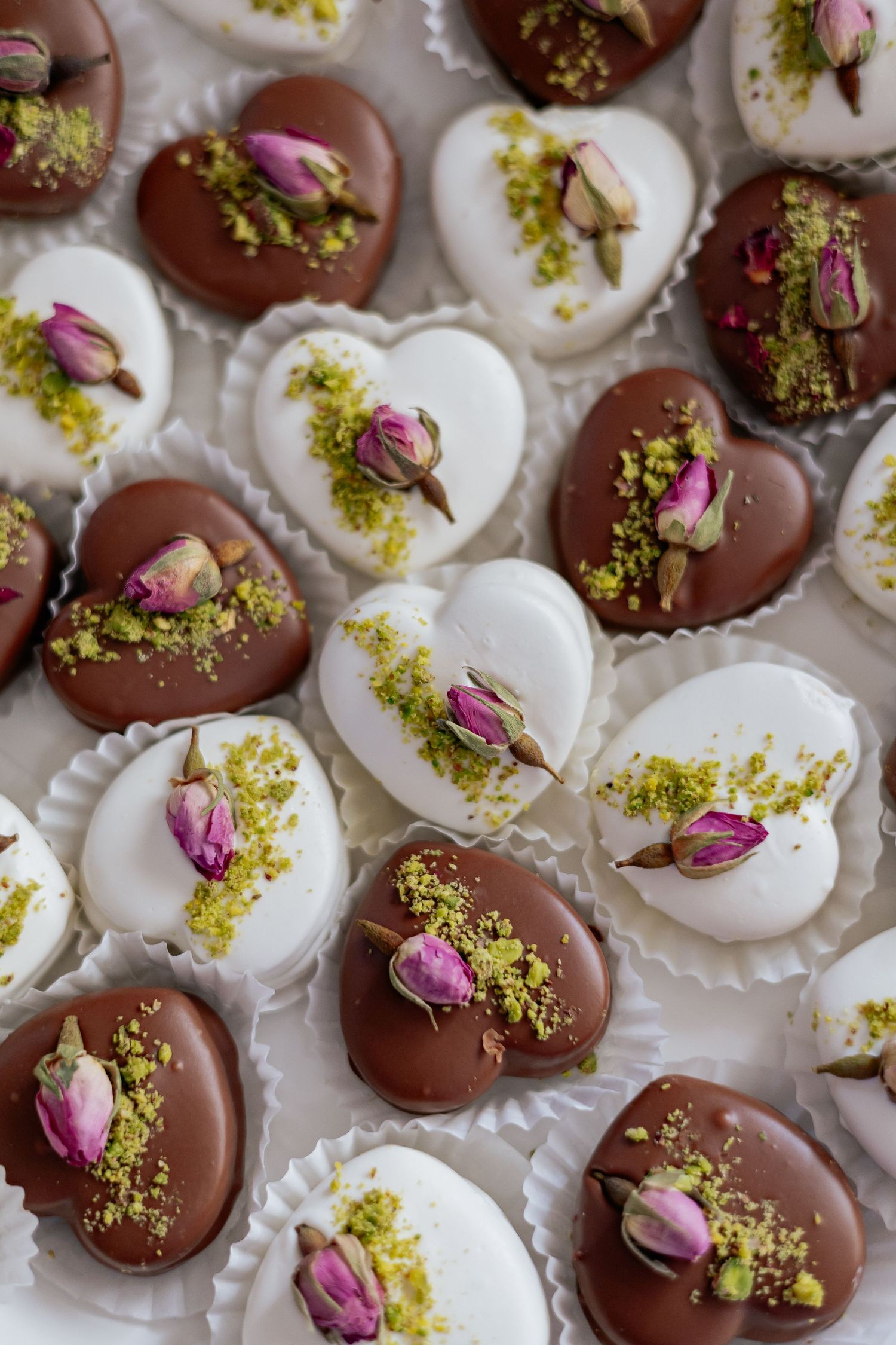 Heart-shaped chocolate and white wedding chocolates topped with dried rose buds and crushed pistachios.