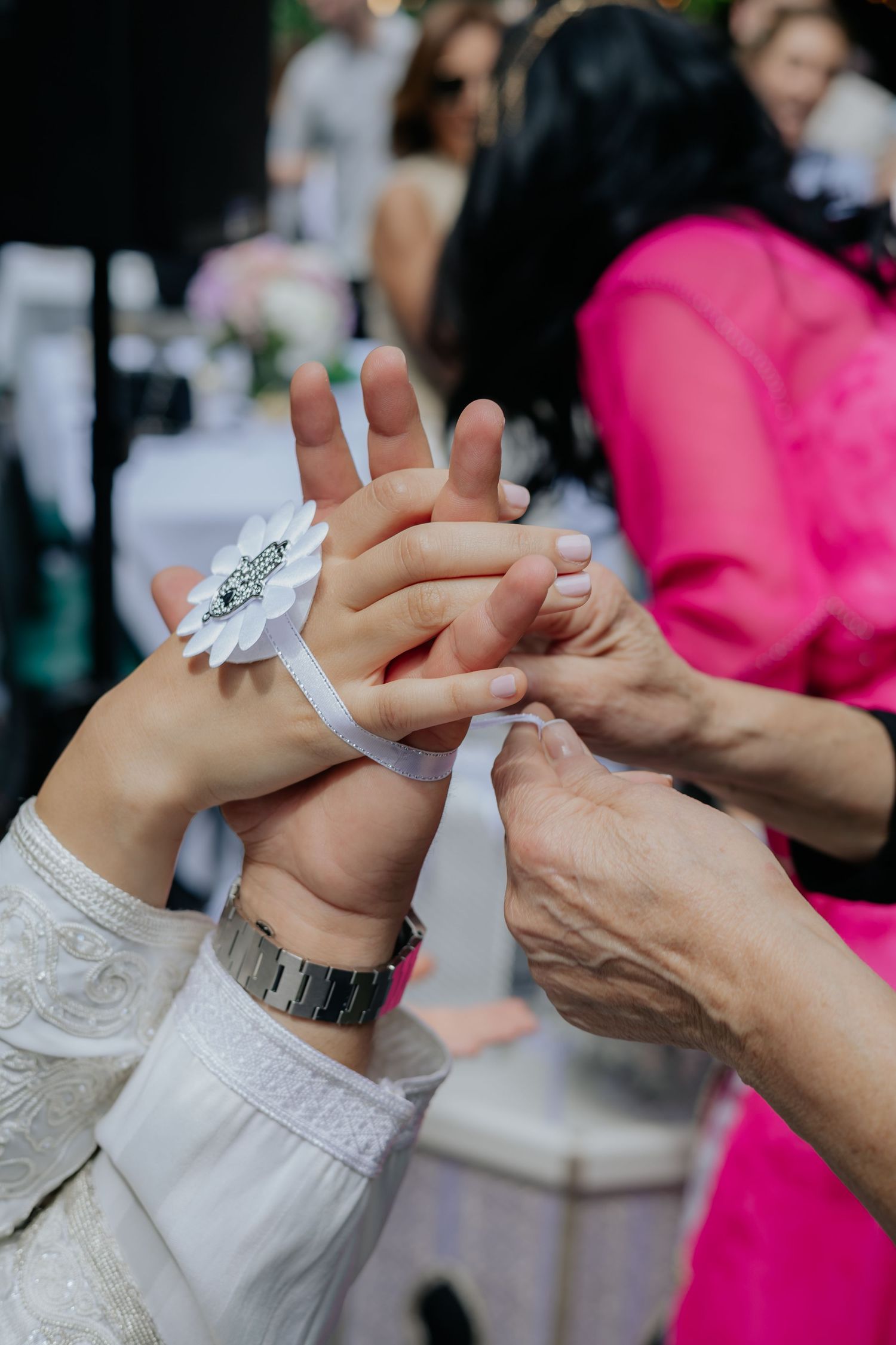 Close-up of hands tying a white floral wrist corsage on bride during traditional Moroccan wedding ceremony.