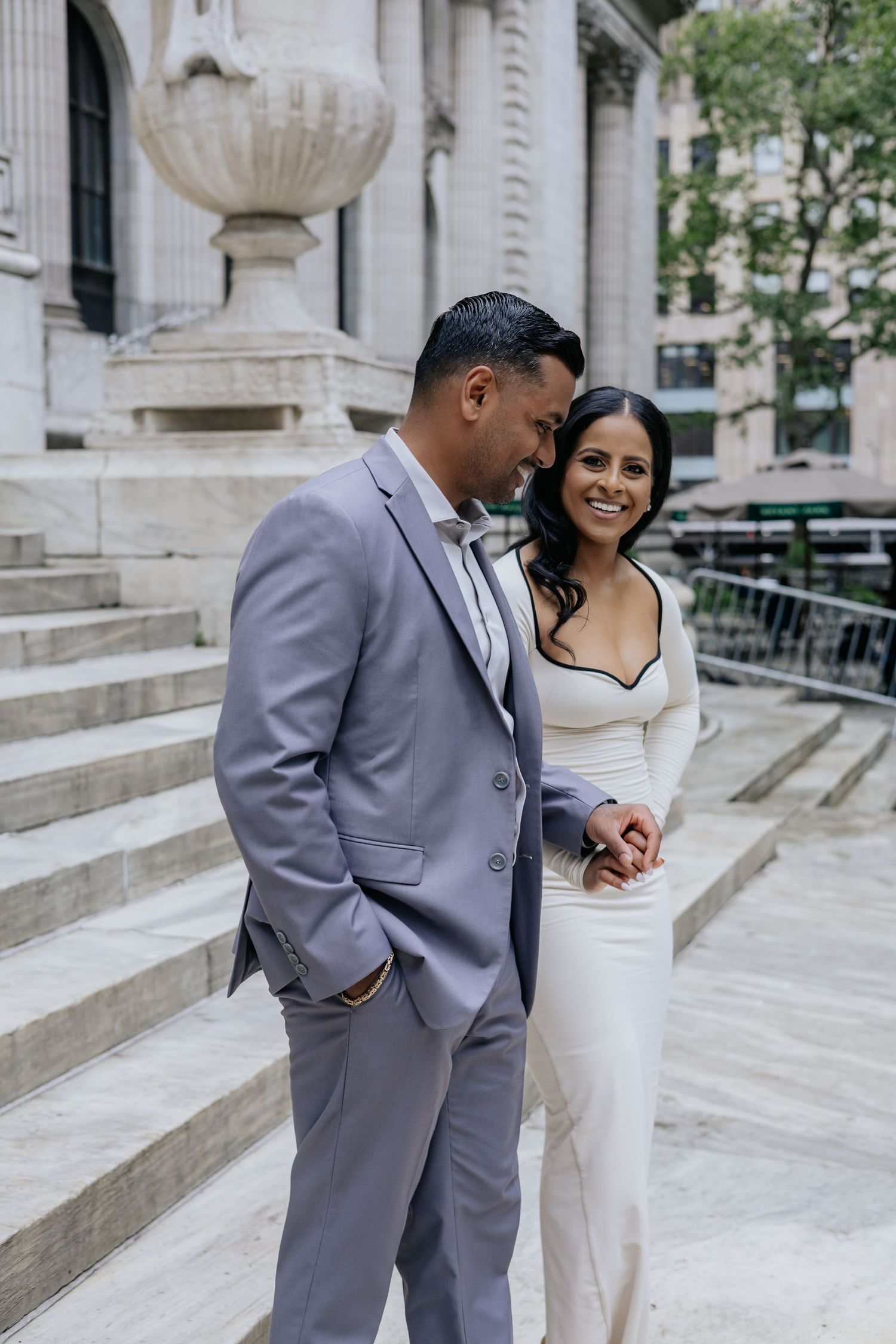 Smiling couple in elegant attire walking down marble steps outside a classic building.
