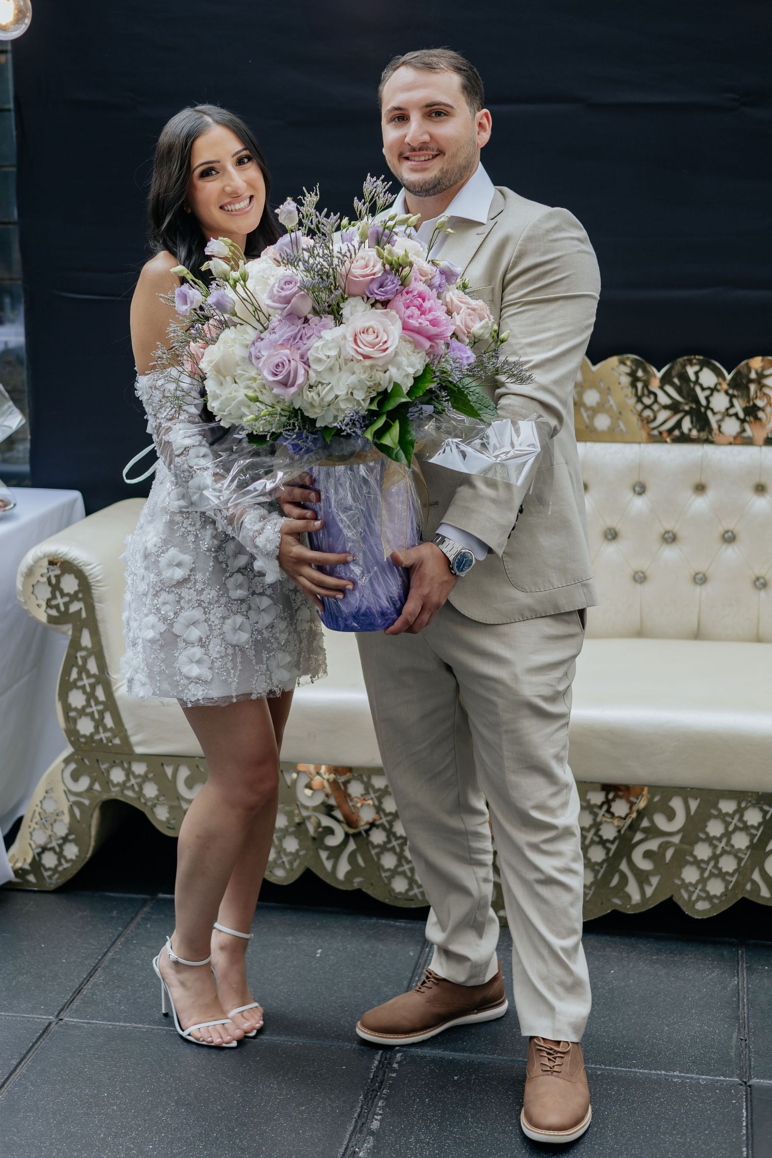 Happy couple posing together holding a large pink and white floral bouquet at their wedding.