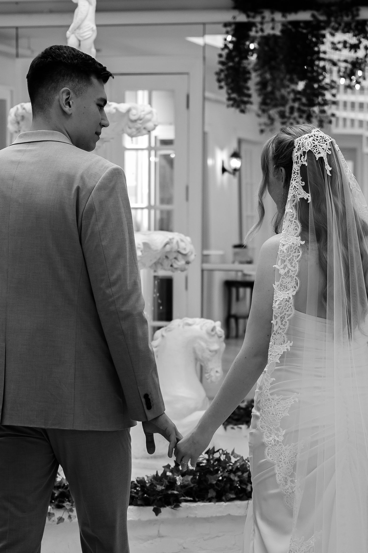 Bride and groom holding hands facing a floral ceremony backdrop, black and white wedding photo.