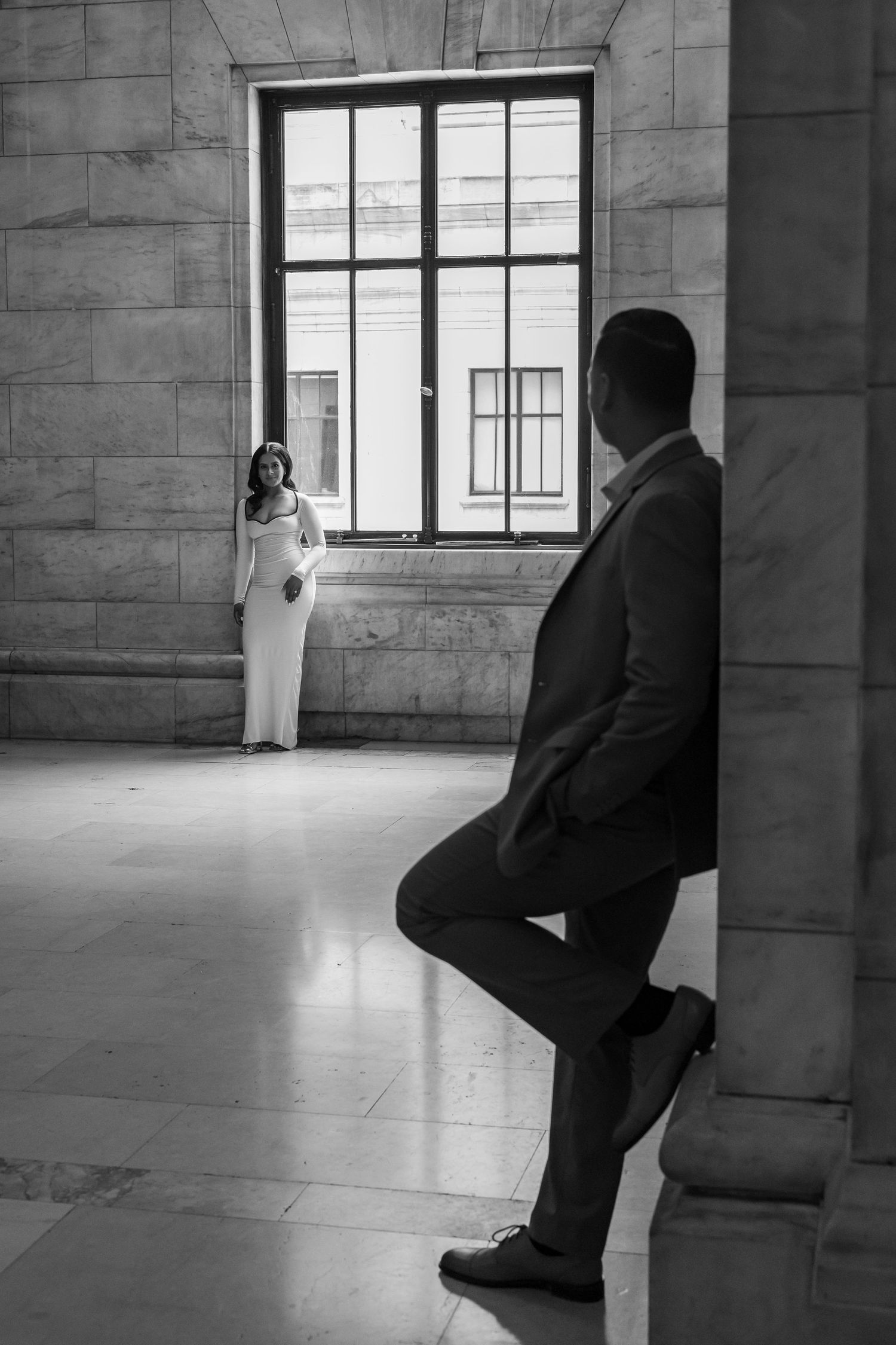 Black and white engagement photo of couple posing in a grand marble hall.