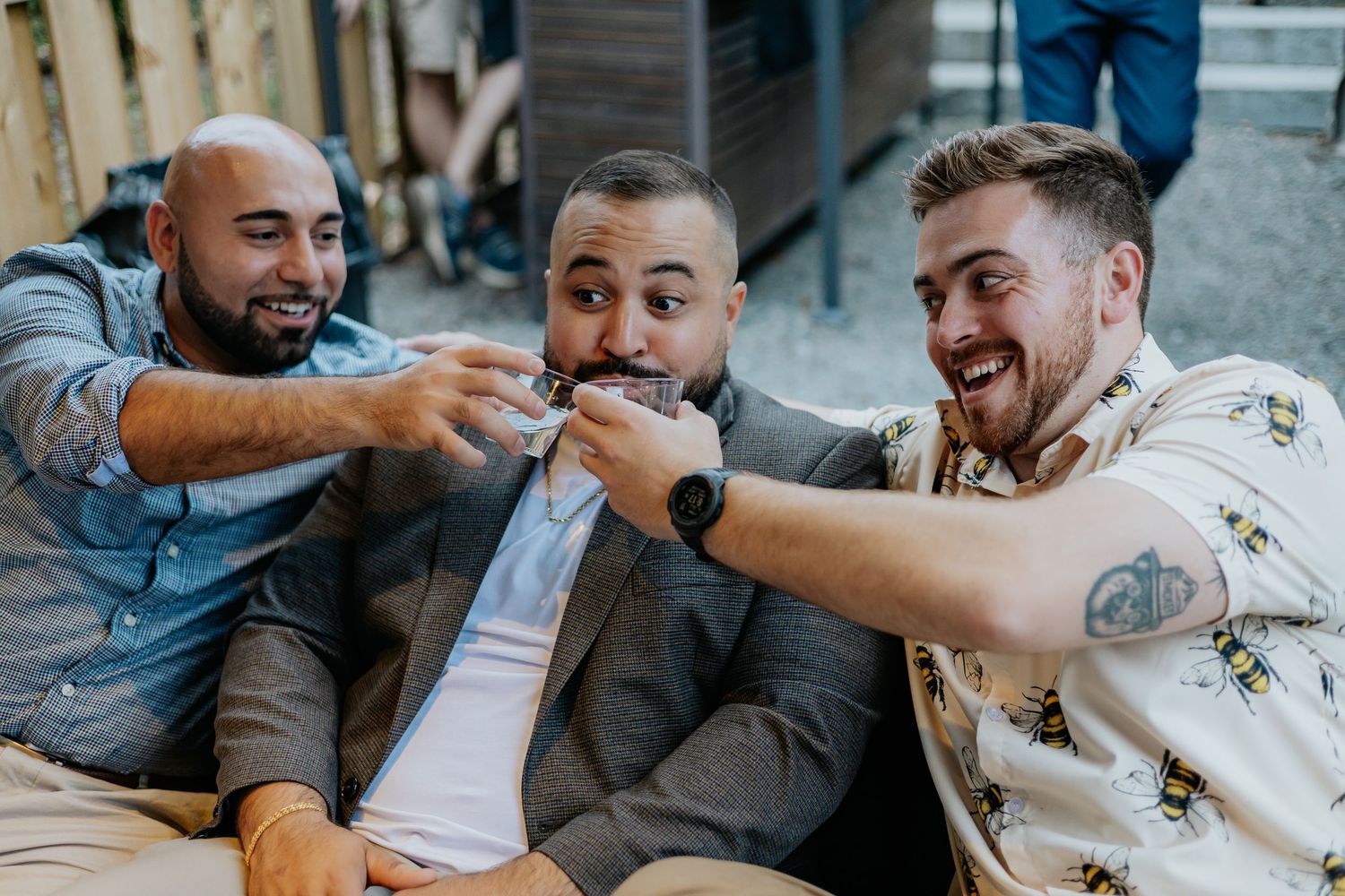 Three men laughing and joking together while seated at a casual outdoor party.