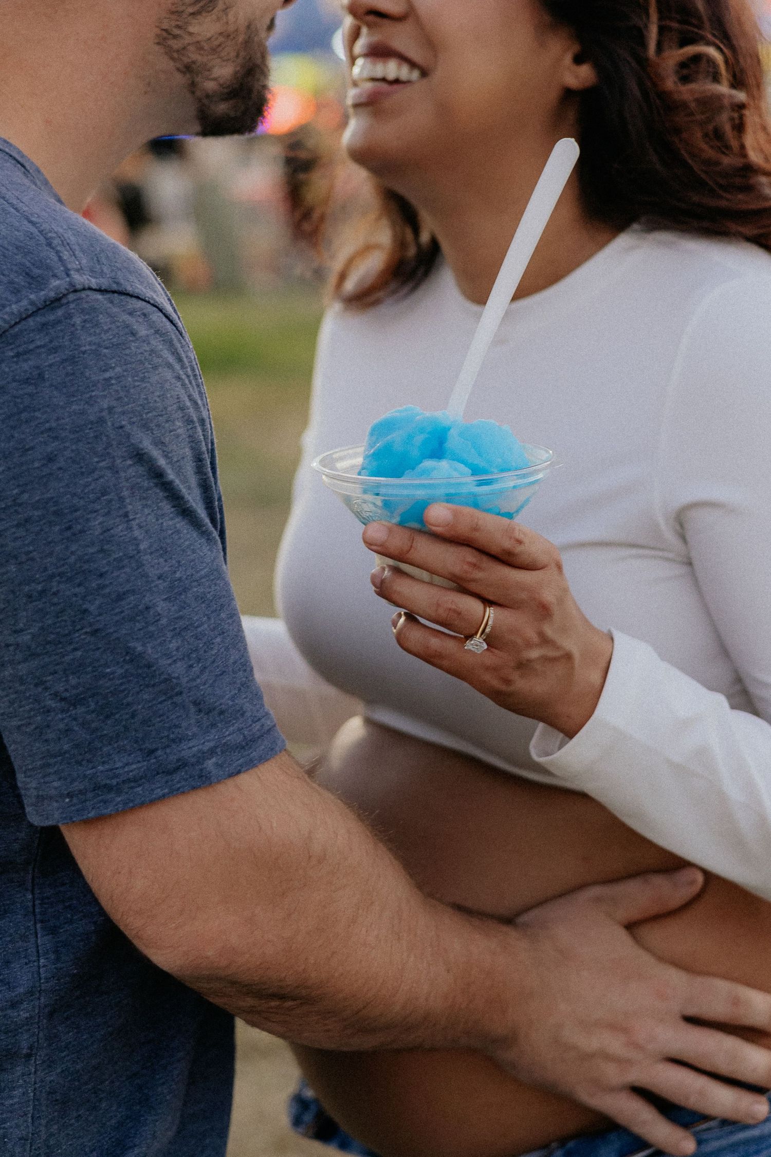 Pregnant woman holding blue shaved ice at a carnival with partner.