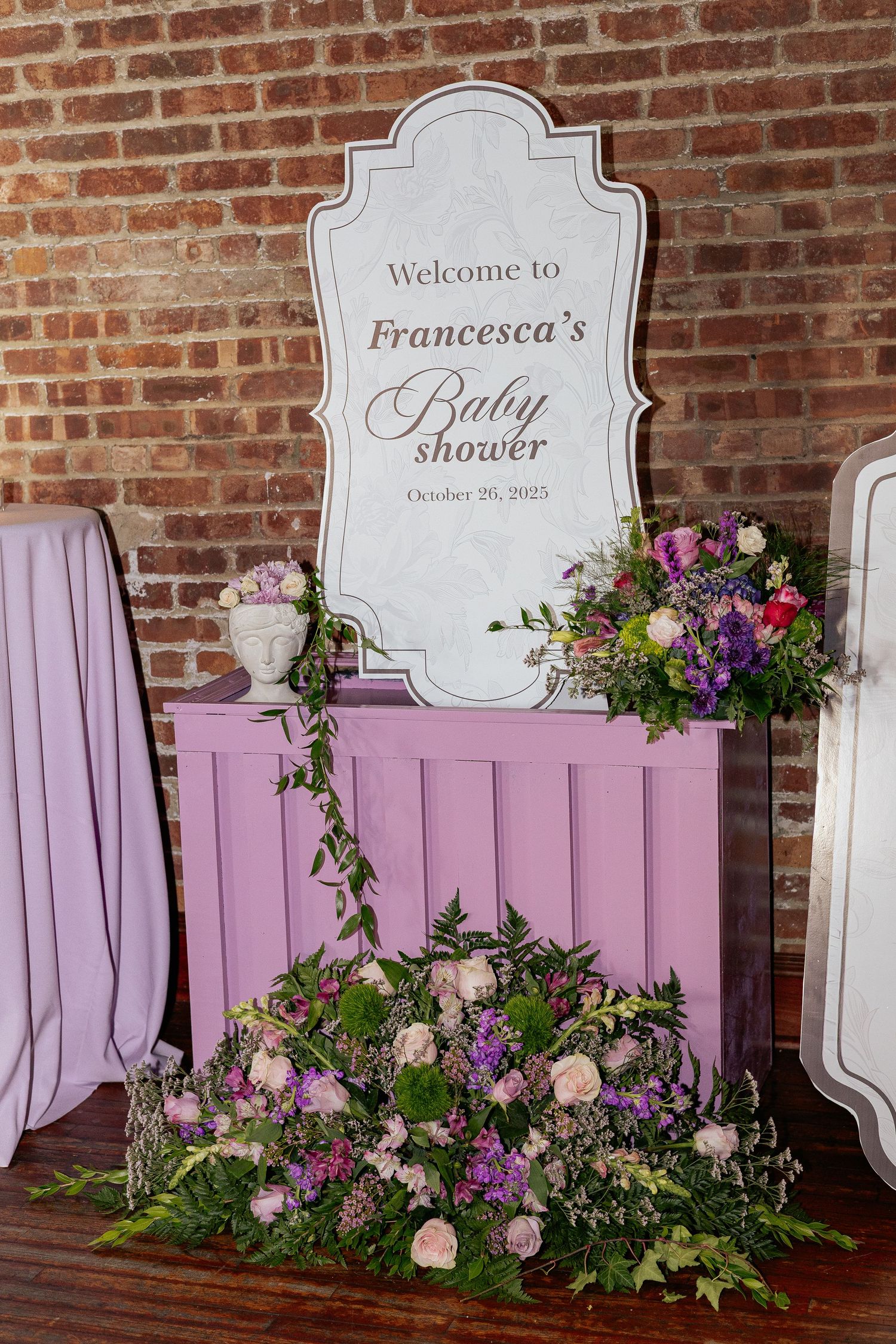 Welcome to Francesca's Baby Shower sign on purple dresser with purple and pink floral arrangements.