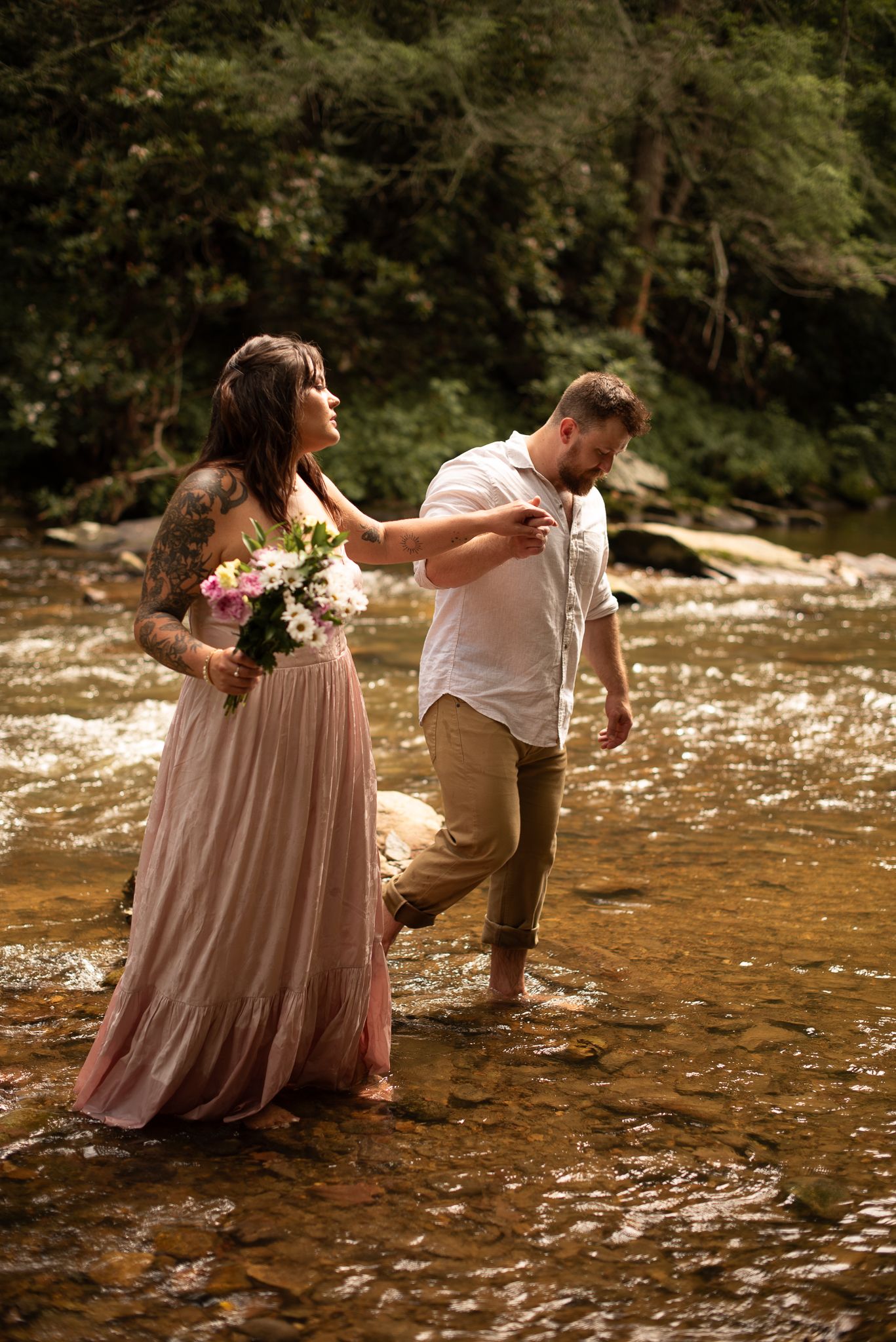 a couple wading in a creek at golden hour