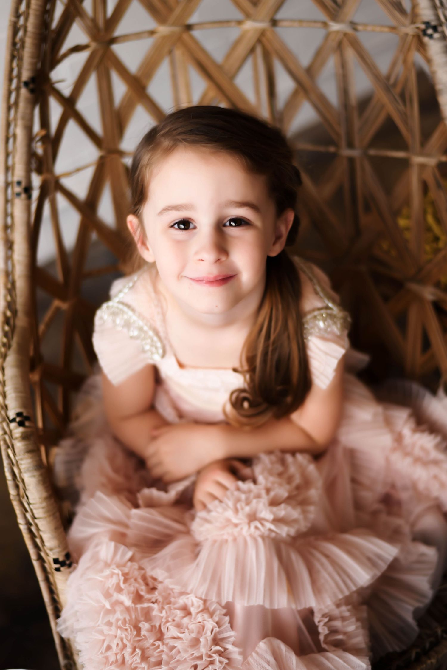 a little girl with a pink ruffled dress sitting in a wicker chair looking up
