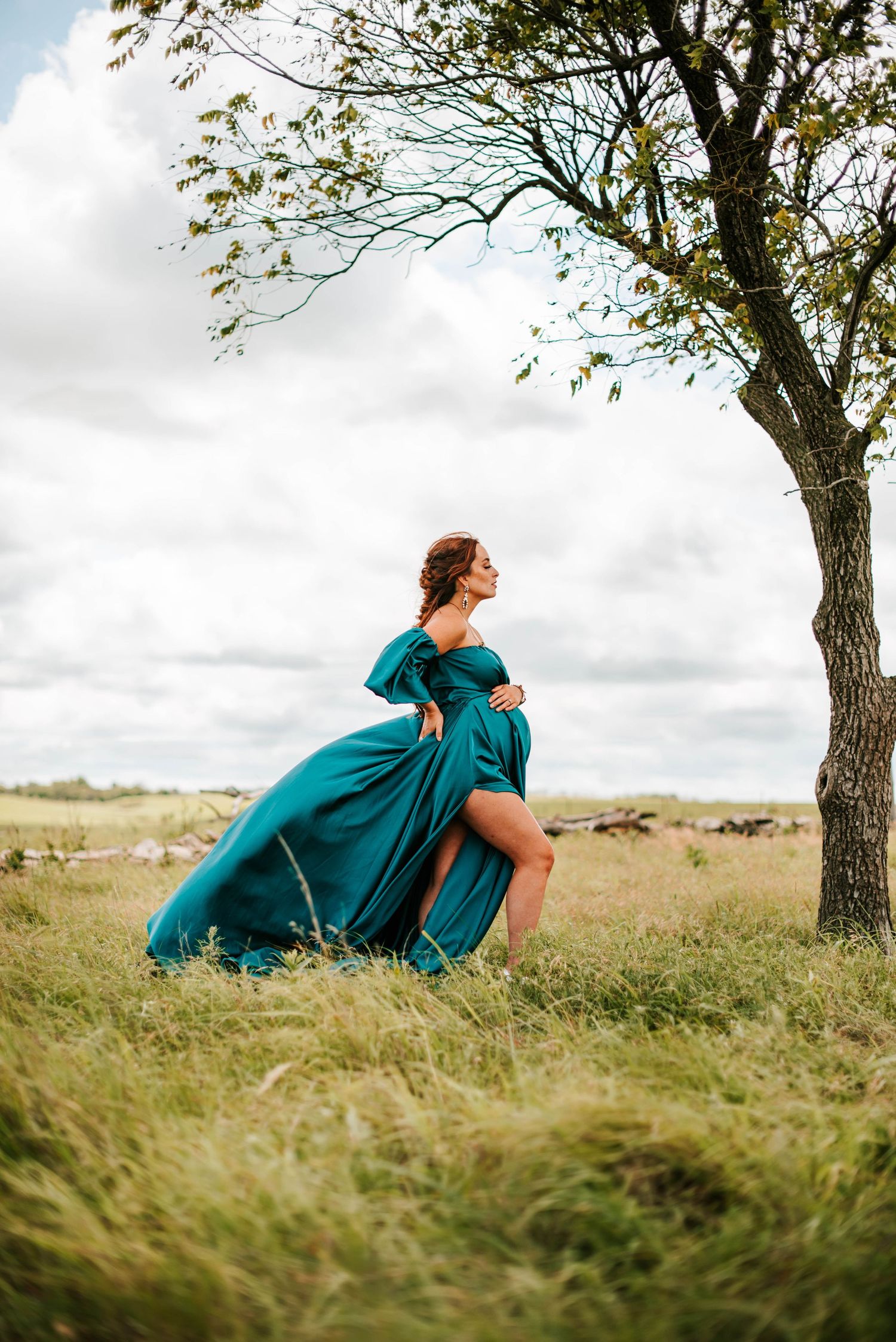 a pregnant woman posing in a green dress beneath a tree