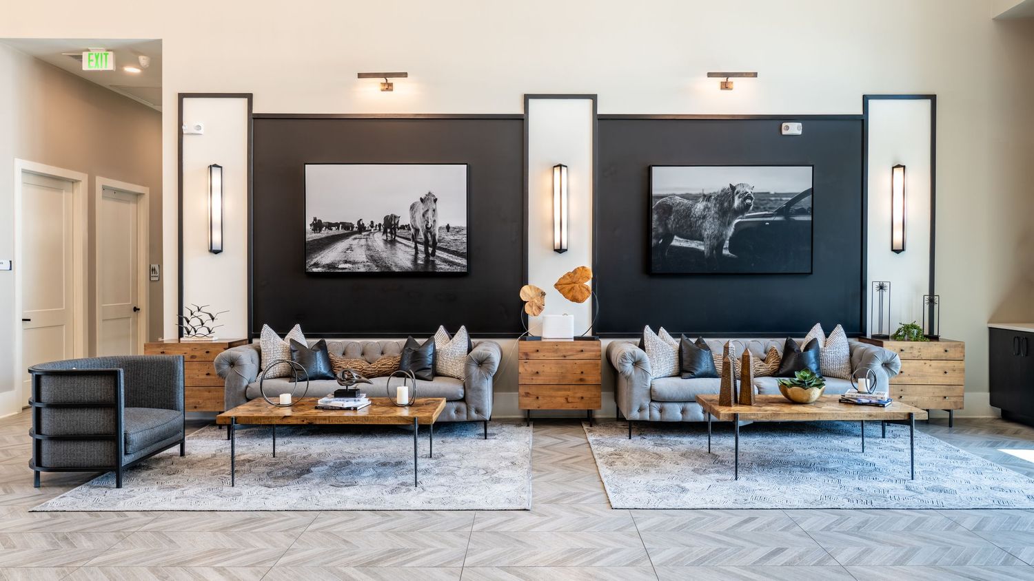 Modern apartment lounge with tufted sofas, wood dressers, herringbone floors, and black-and-white photography wall art.