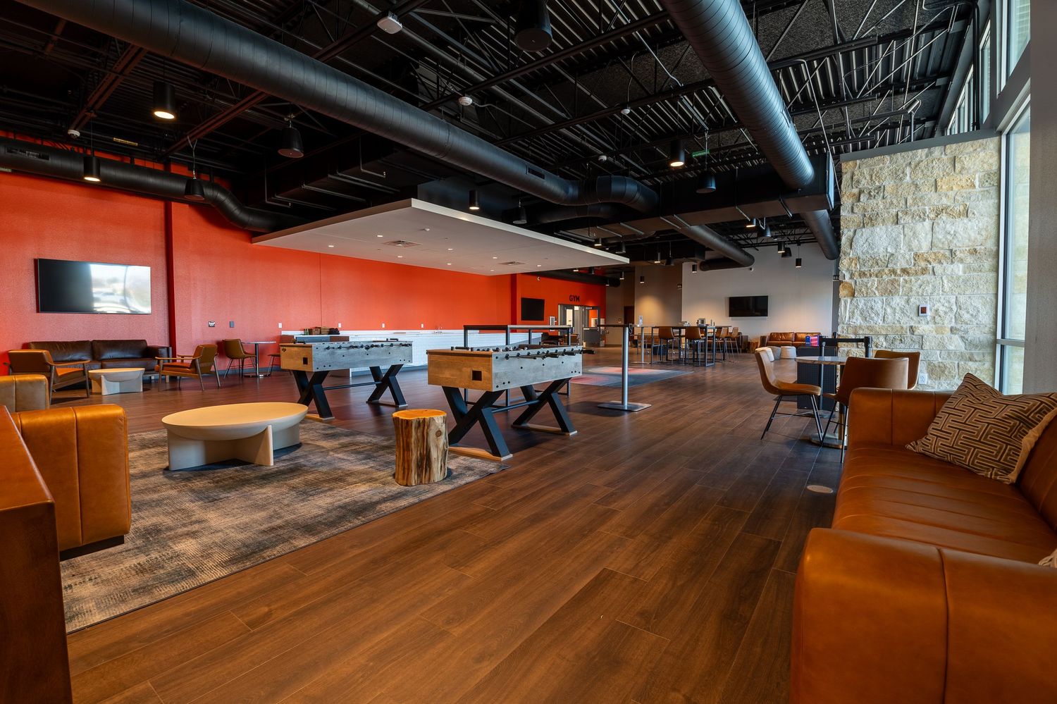 Modern industrial office space with exposed ceiling, concrete floors, and orange lounge seating in an open layout design.