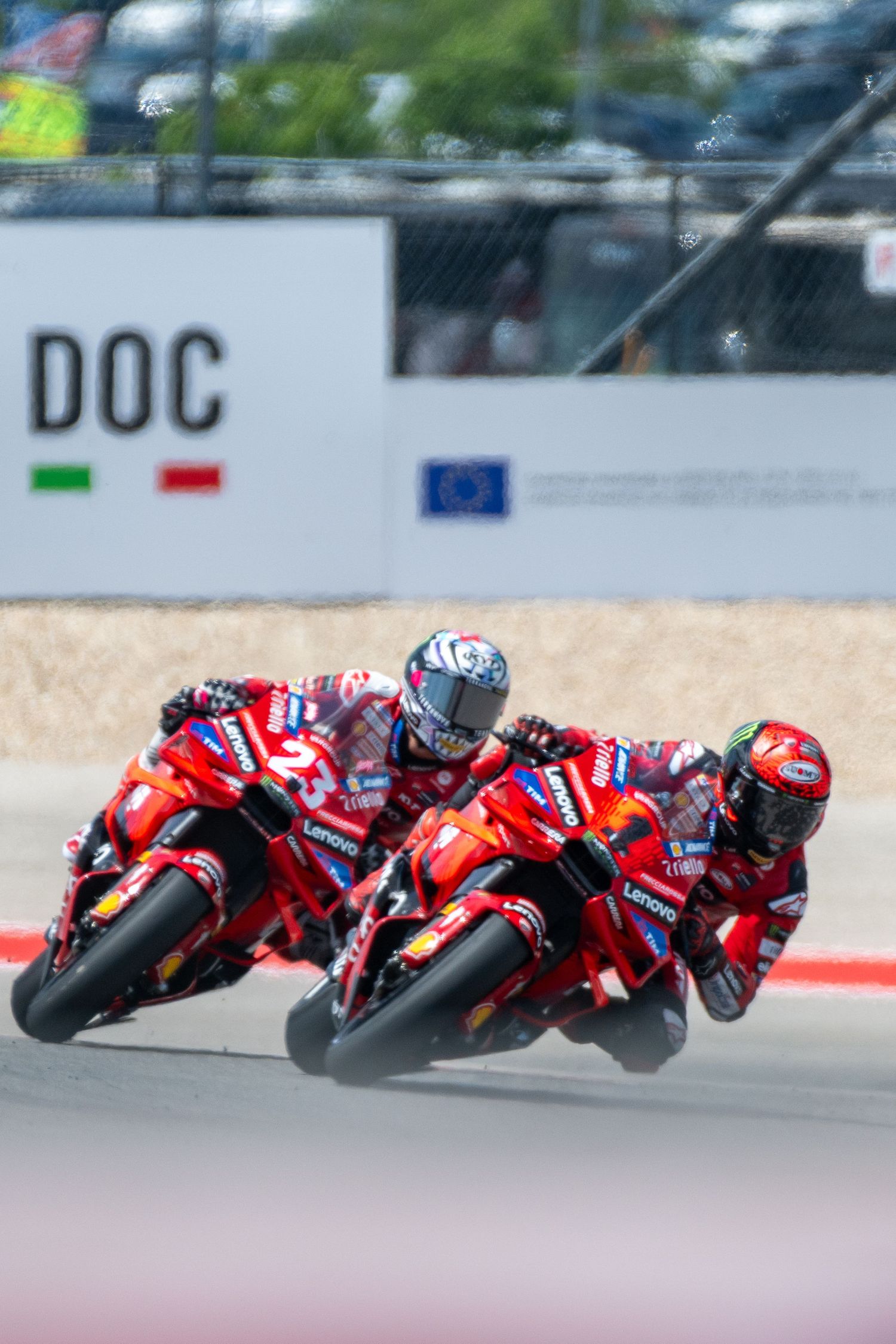 Row of red racing motorcycles leaning into turn during professional MotoGP race.