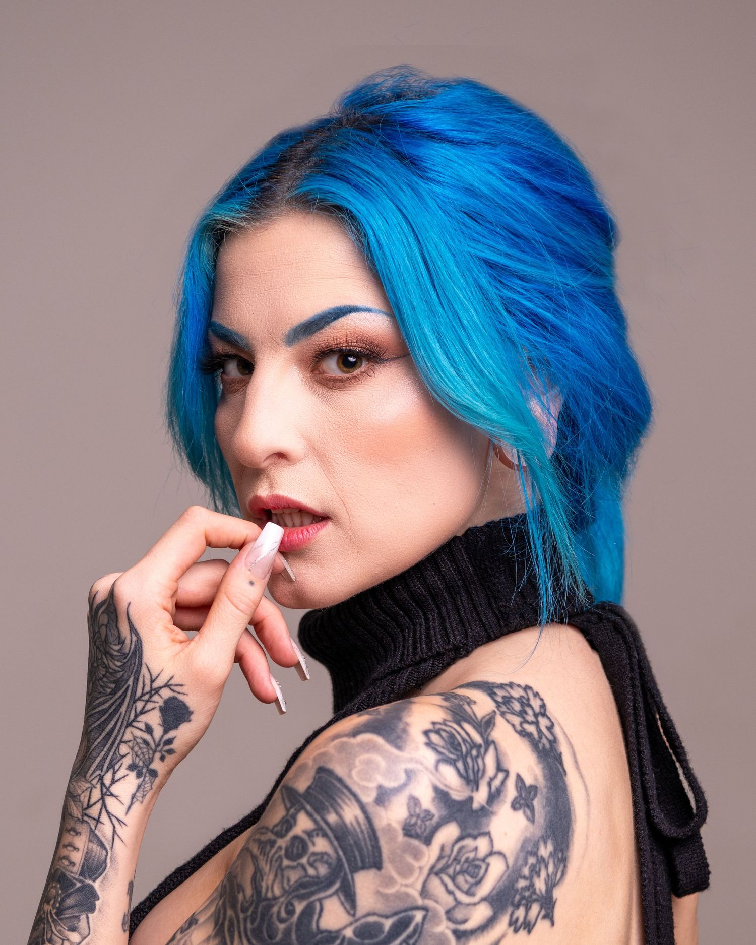 Woman with blue hair and tattoos posing in a black turtleneck top, holding a cigarette.