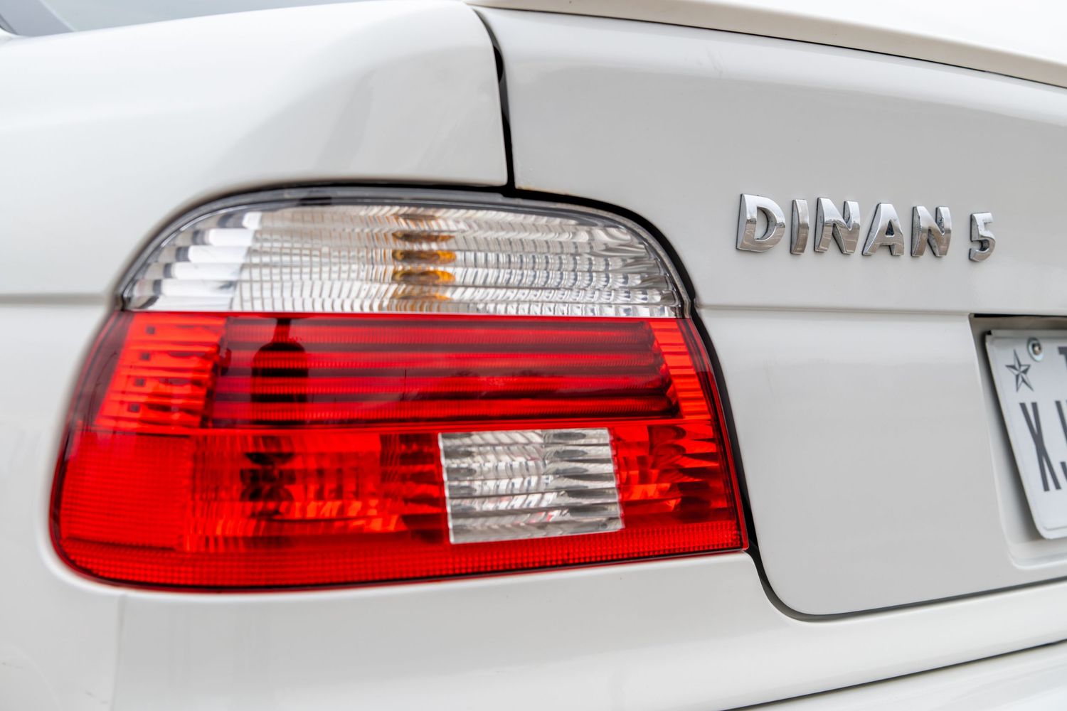 Close-up of a BMW Dinan 5 rear tail light on a white sedan, showcasing red and clear lens design.