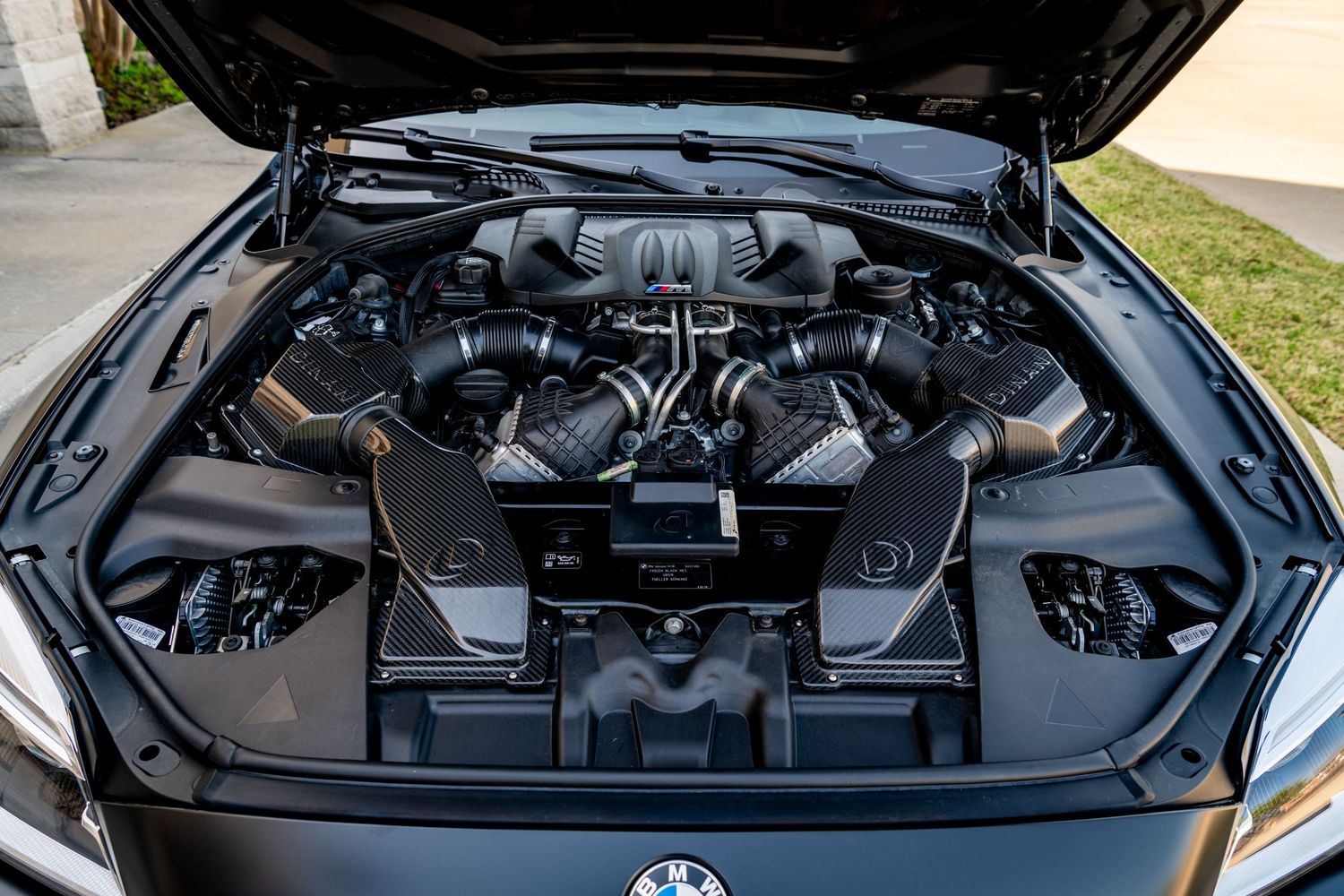 BMW high-performance V8 engine bay with carbon fiber intake components and twin-turbo setup visible under open hood.