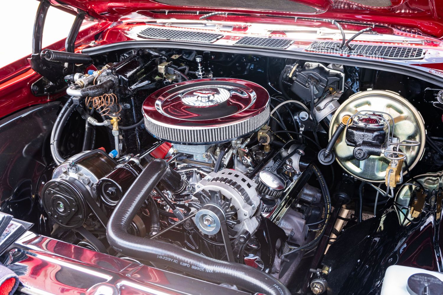 Classic car V8 engine bay with chrome air cleaner, alternator, and polished components in a vintage red vehicle.
