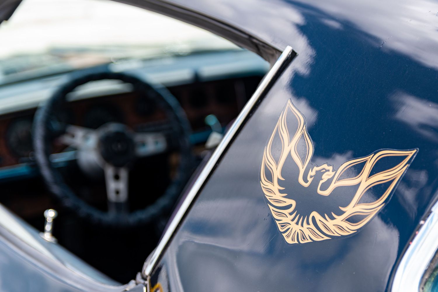 Gold Firebird emblem on a dark blue Pontiac Trans Am dashboard with steering wheel visible in background.