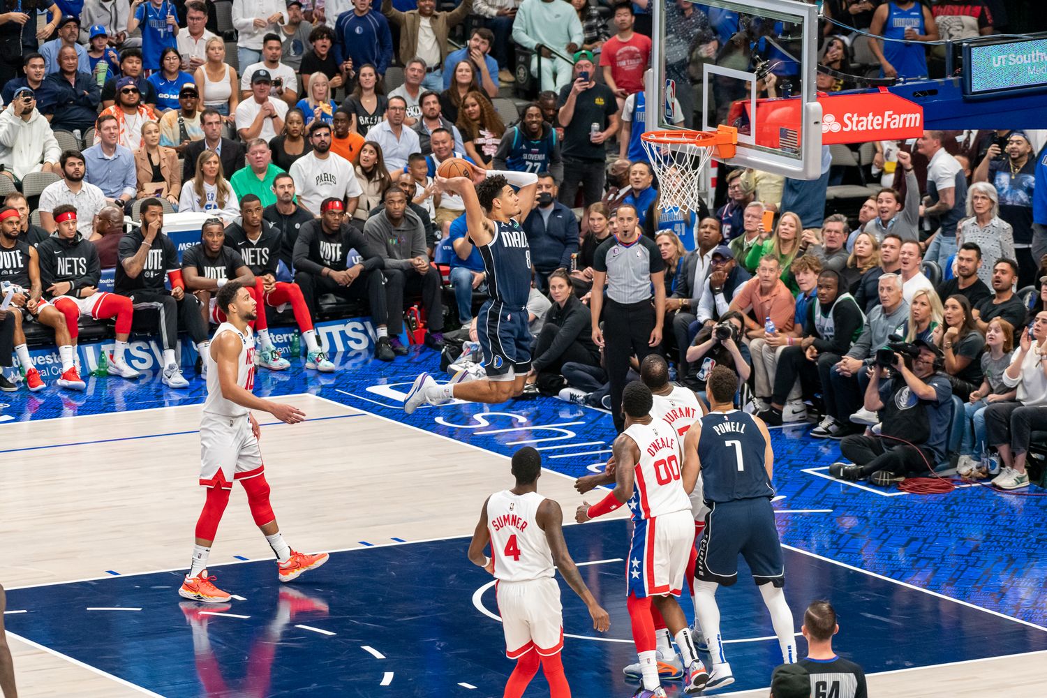 Professional basketball players compete during an intense game at a packed indoor arena.