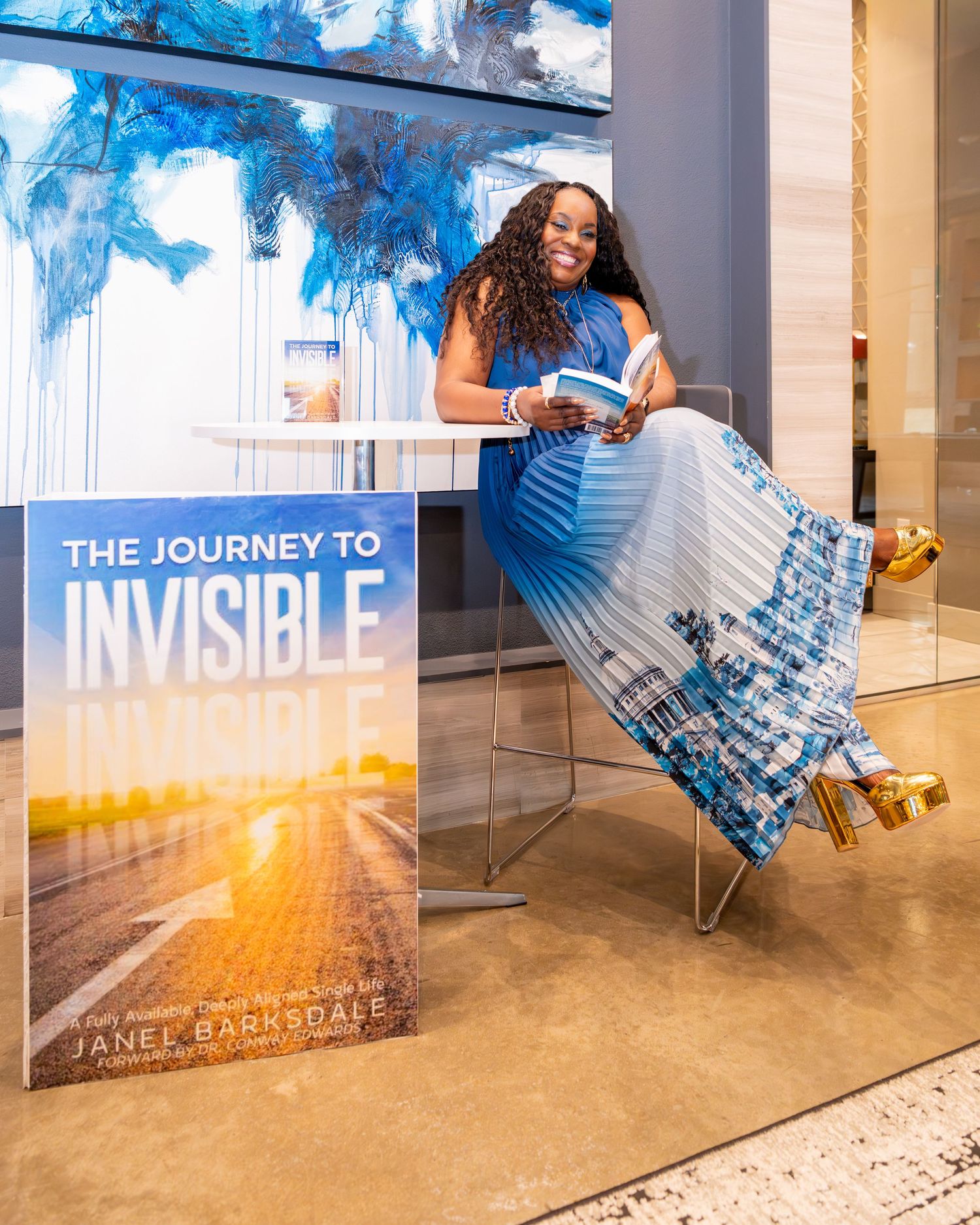 Author Janel Barksdale smiles beside her book 'The Journey to Invisible' at a bright, modern book signing event.