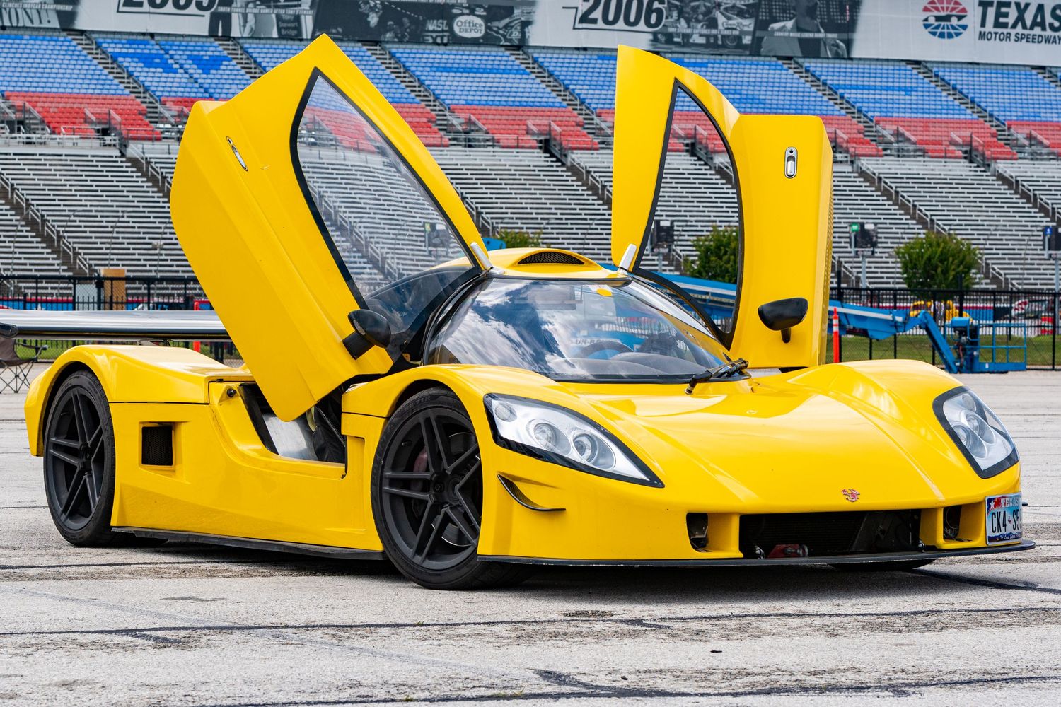 Yellow supercar with scissor doors open at Texas Motor Speedway, showcasing its exotic low-profile design.