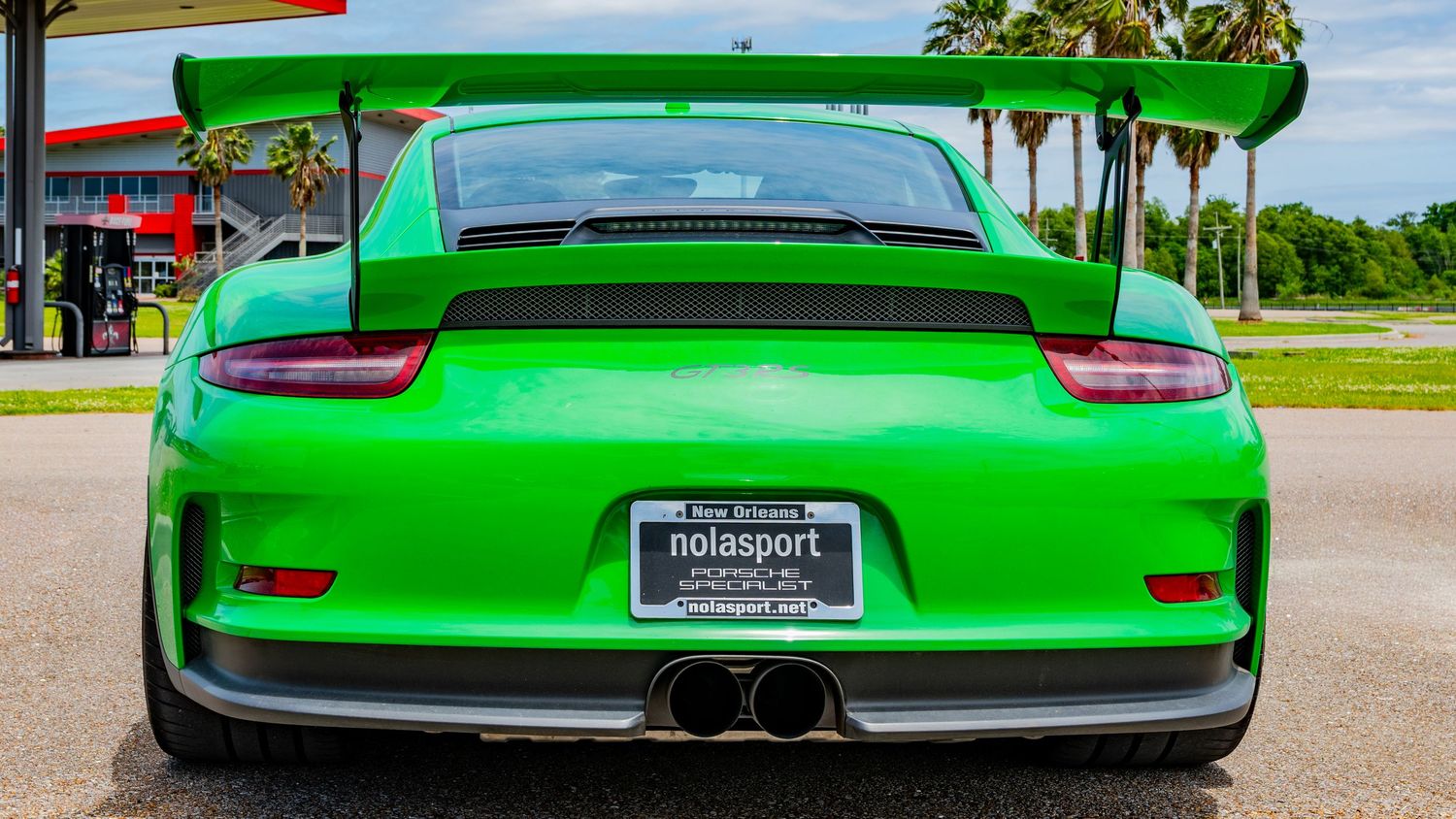 Rear view of a vibrant green Porsche 911 GT3 RS sports car parked outdoors near palm trees.