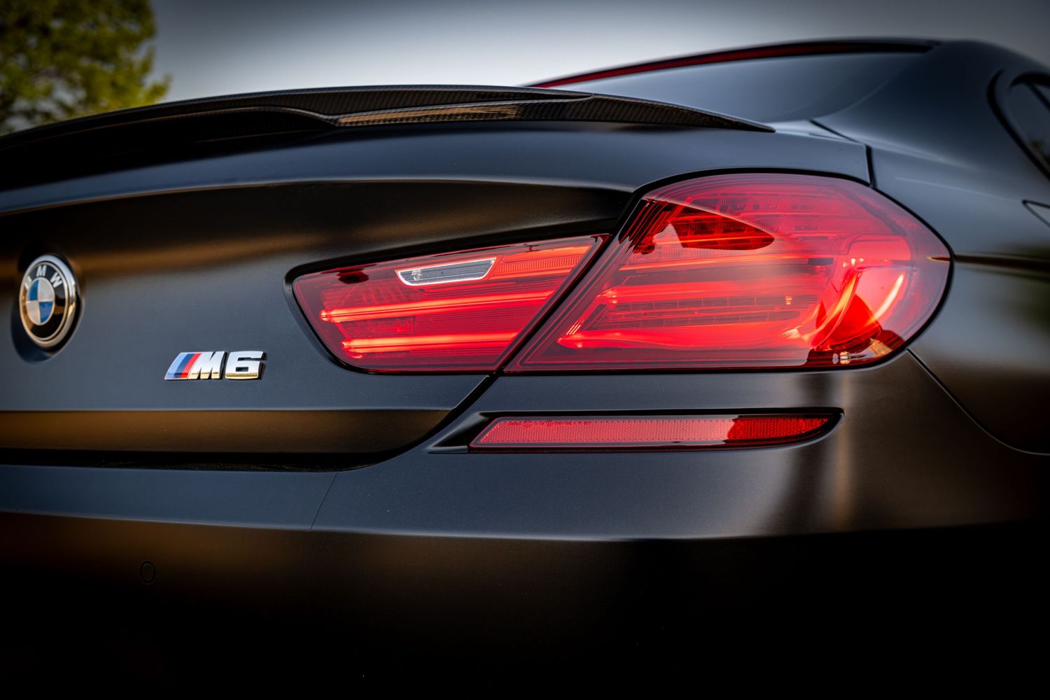 Close-up of a BMW M6 rear badge and tail light on a sleek dark luxury sports car.