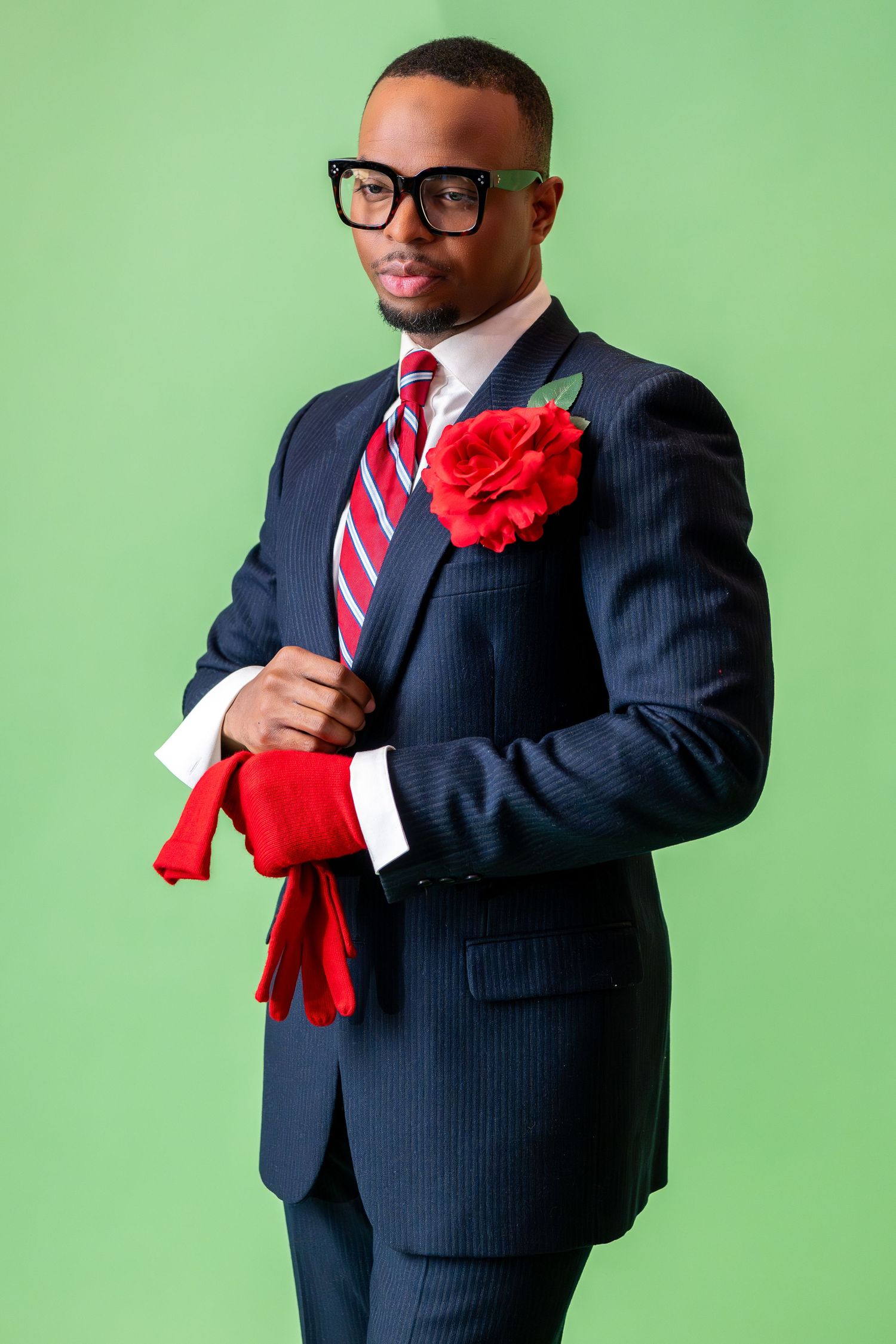 Professional wearing a navy pinstripe suit with glasses, red striped tie and red flower boutonniere against green background.