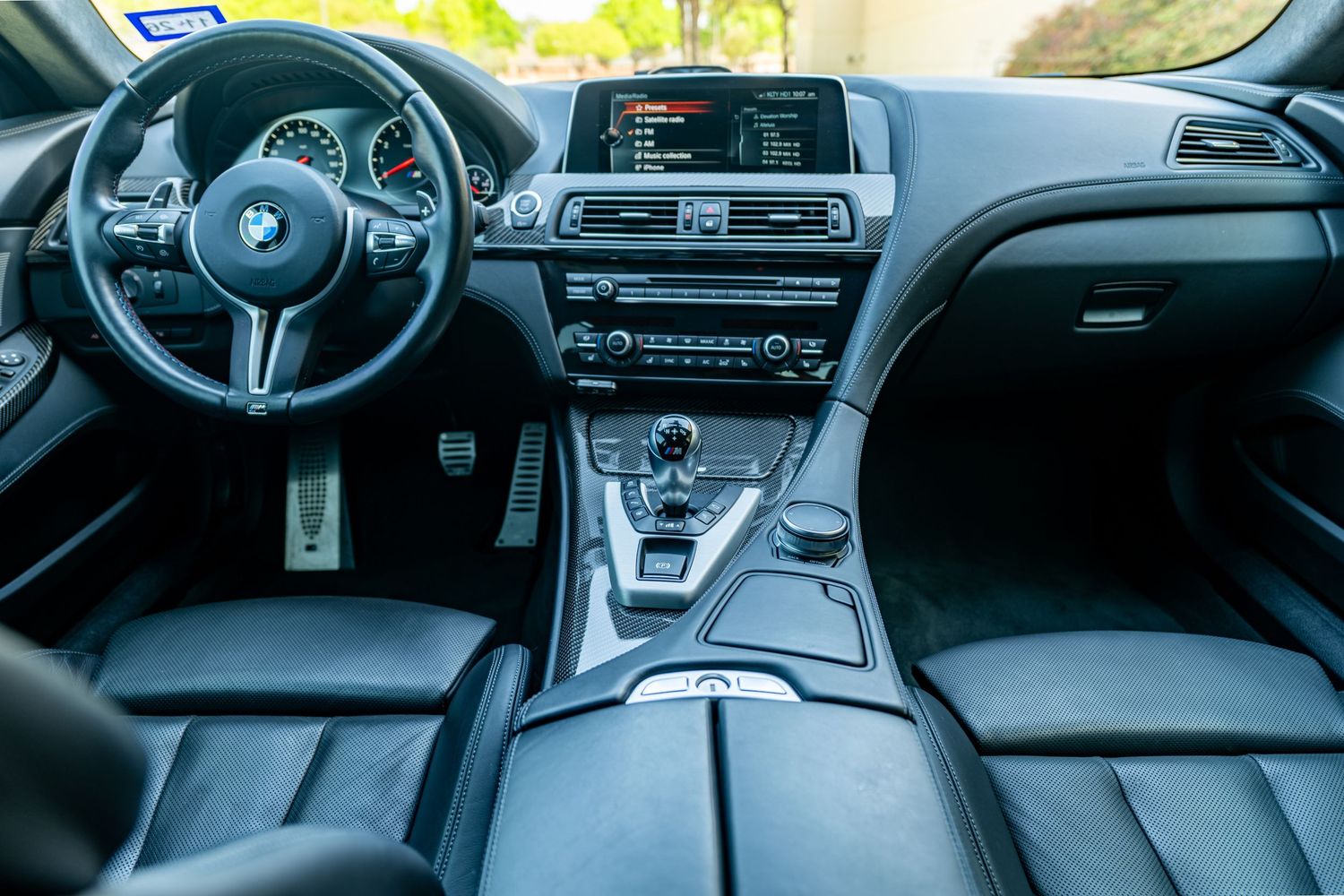 BMW luxury car interior featuring black leather seats, M-sport steering wheel, iDrive infotainment screen, and carbon fiber trim.
