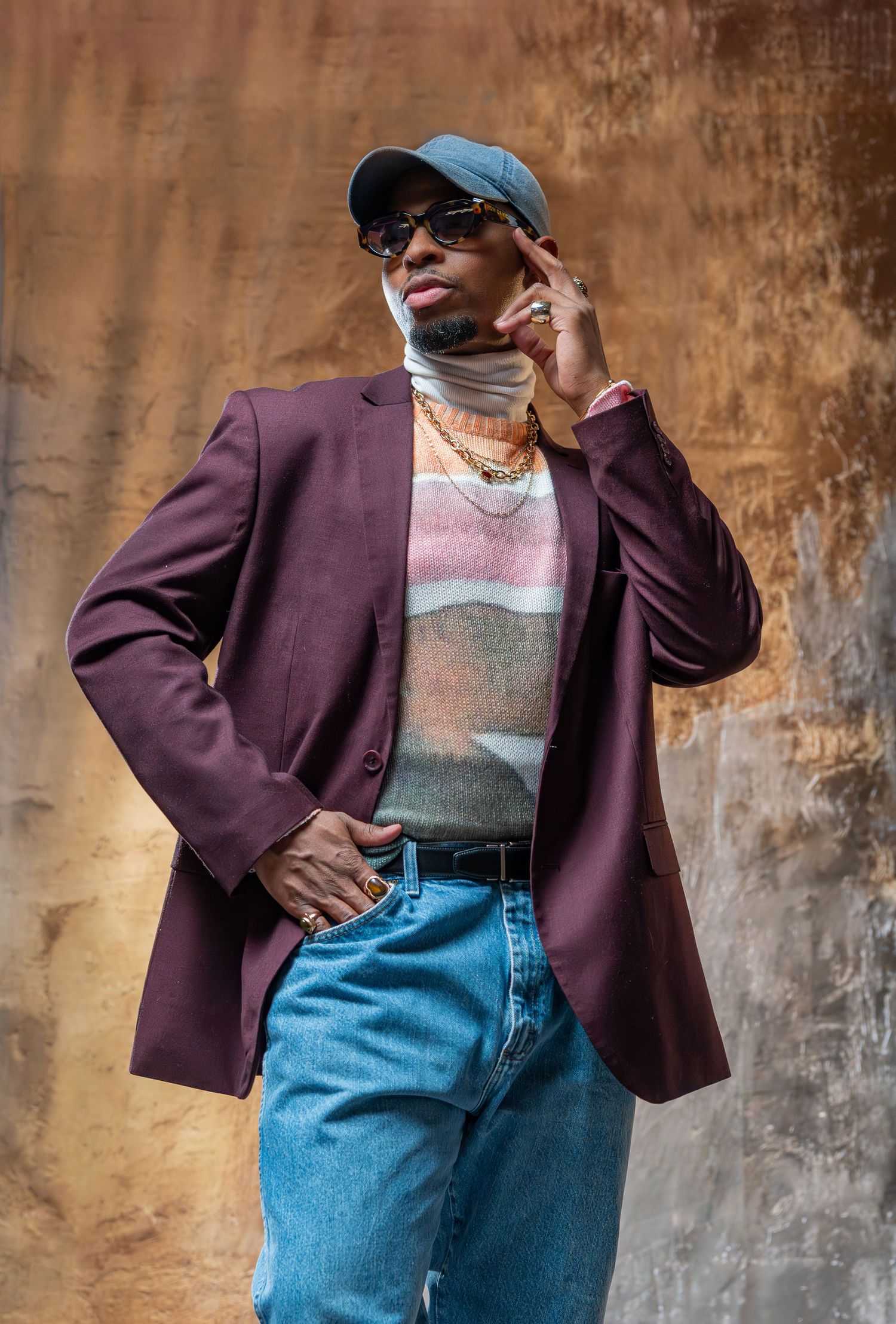 A fashion collage showing a burgundy blazer styled with blue jeans and sunglasses against a textured brown wall.