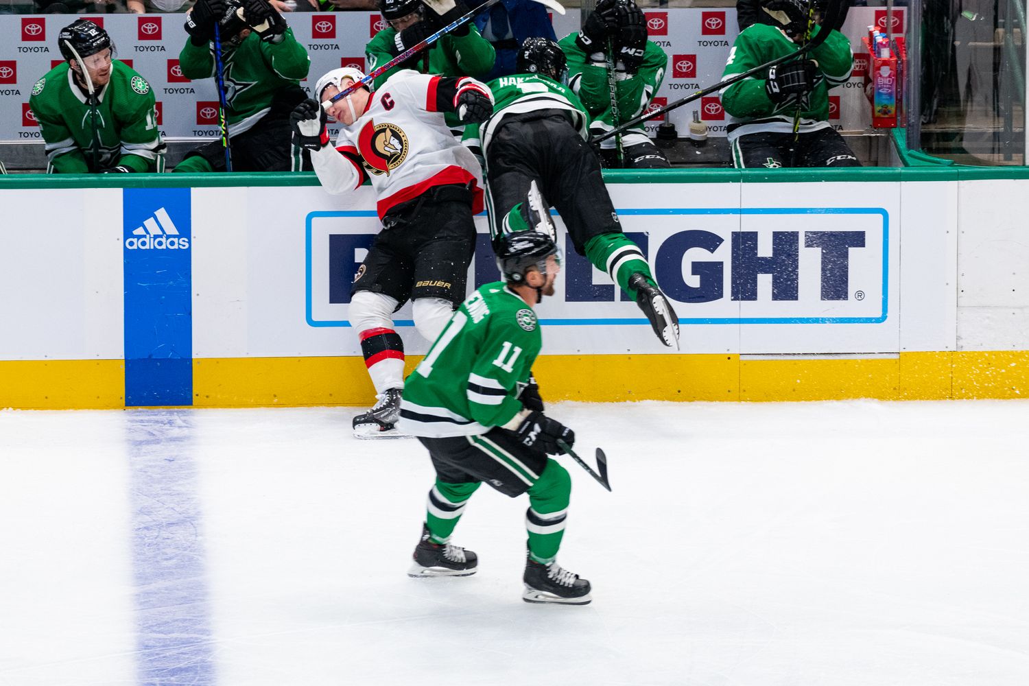 Hockey players in green and white jerseys battle for position during intense game action.