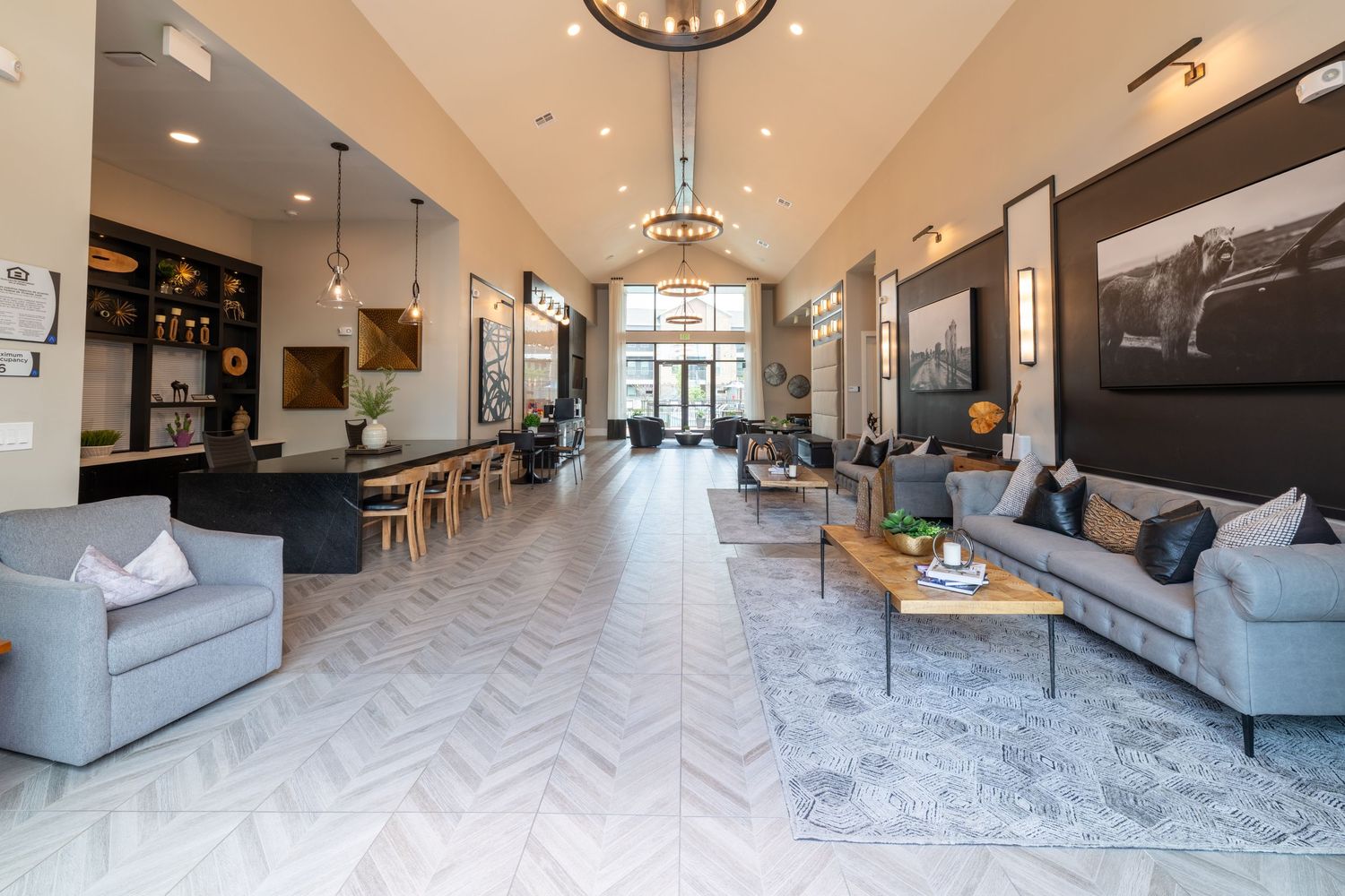 Elegant apartment lobby with herringbone floors, gray sofas, chandelier, and open bar area in modern design.