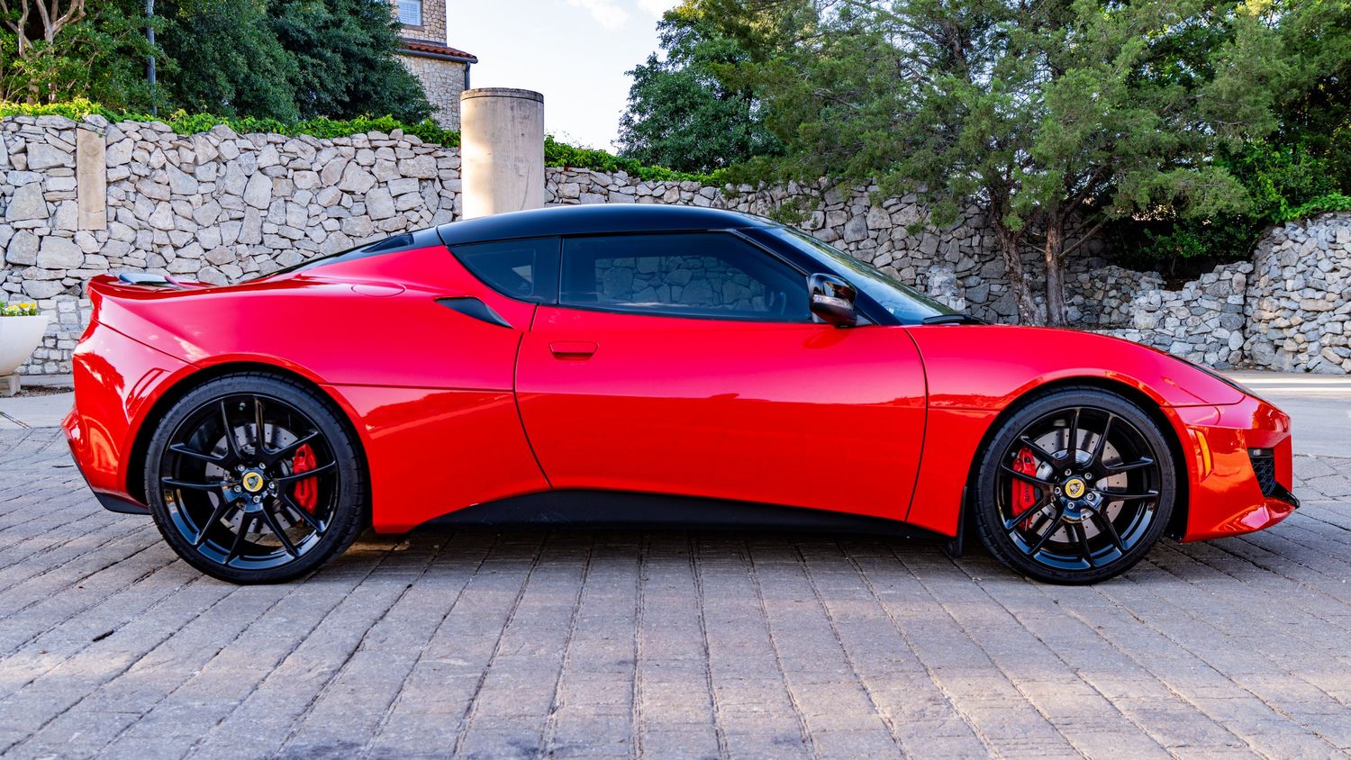 Red Lotus Evora sports car parked outdoors, showcasing sleek aerodynamic design and black alloy wheels.