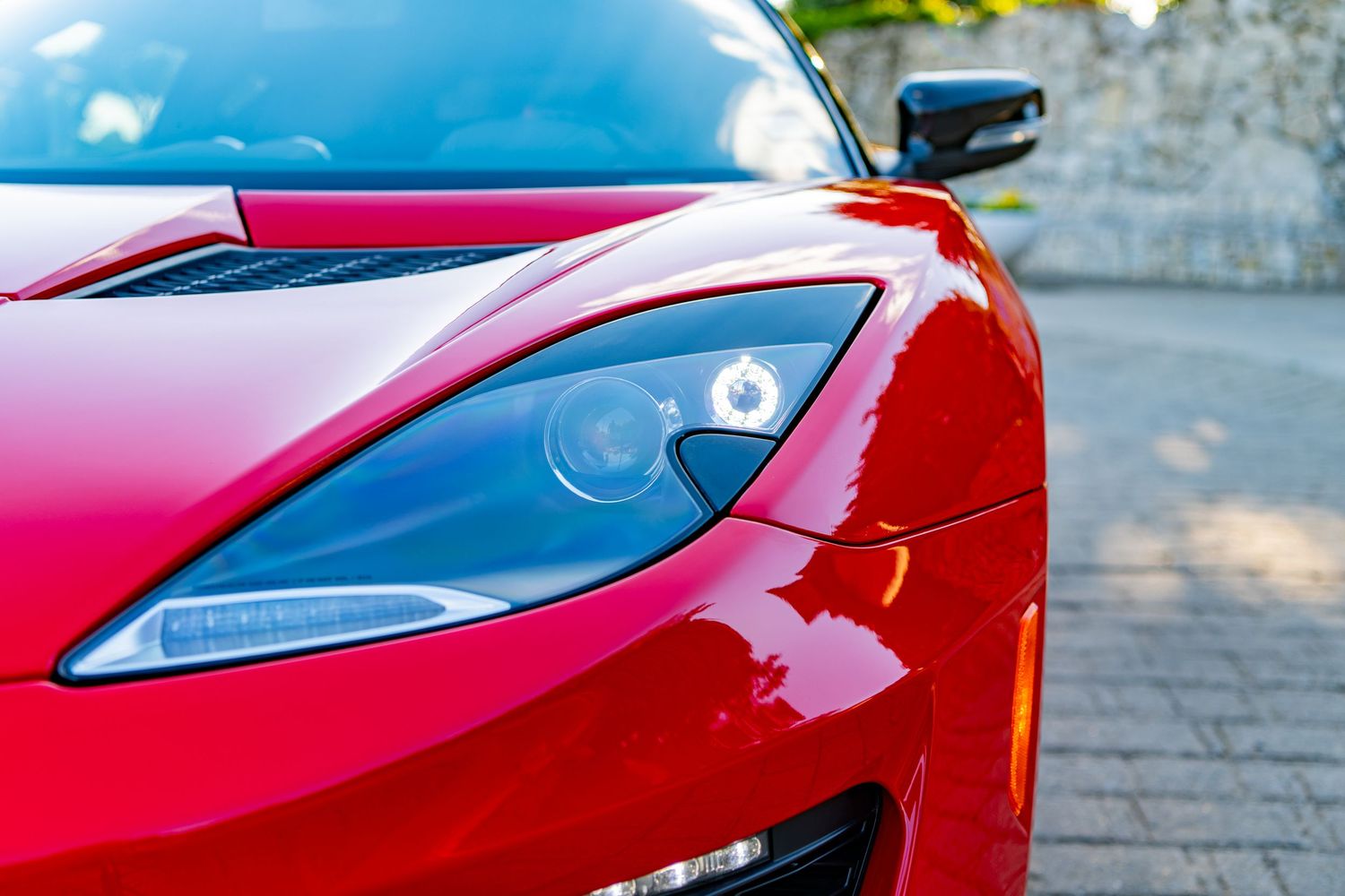 Close-up of a sleek red sports car headlight with chrome detailing, showcasing the aerodynamic design of a luxury vehicle.