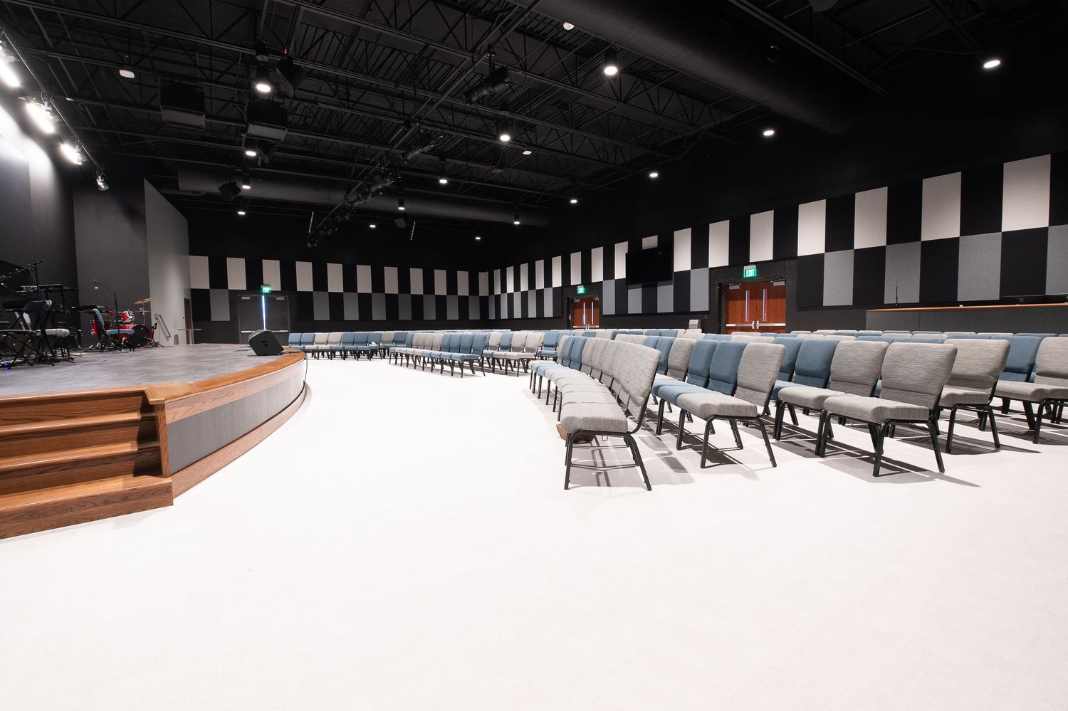 Modern auditorium interior with black seats arranged in curved rows and illuminated by overhead spotlights.