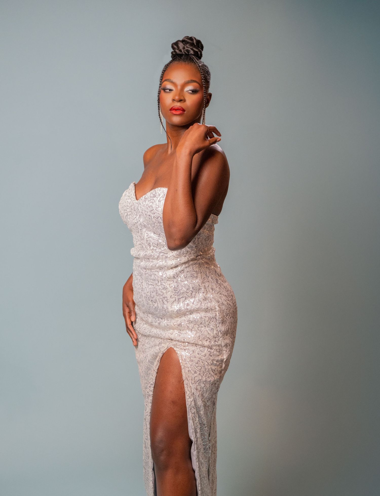 Woman in a sequined strapless gown with a thigh-high slit poses elegantly against a soft gray background.