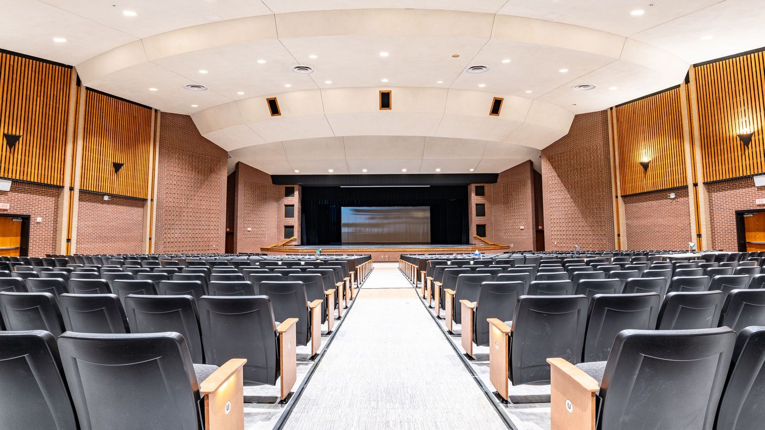 Theater auditorium with curved ceiling and rows of dark seats leading to stage.