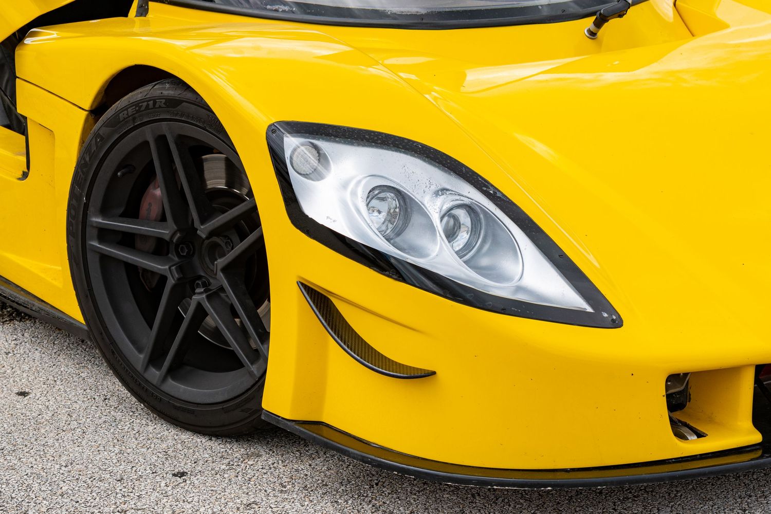 Close-up of a yellow supercar's front wheel, headlight, and aerodynamic bodywork on a paved surface.