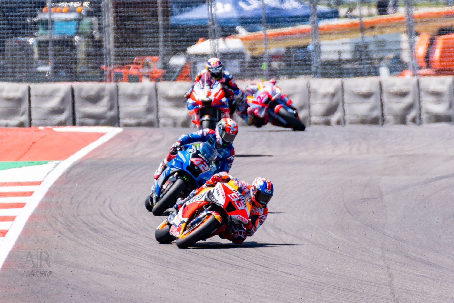 Motorcycle racers lean into a tight corner during a MotoGP race on a professional racing circuit.